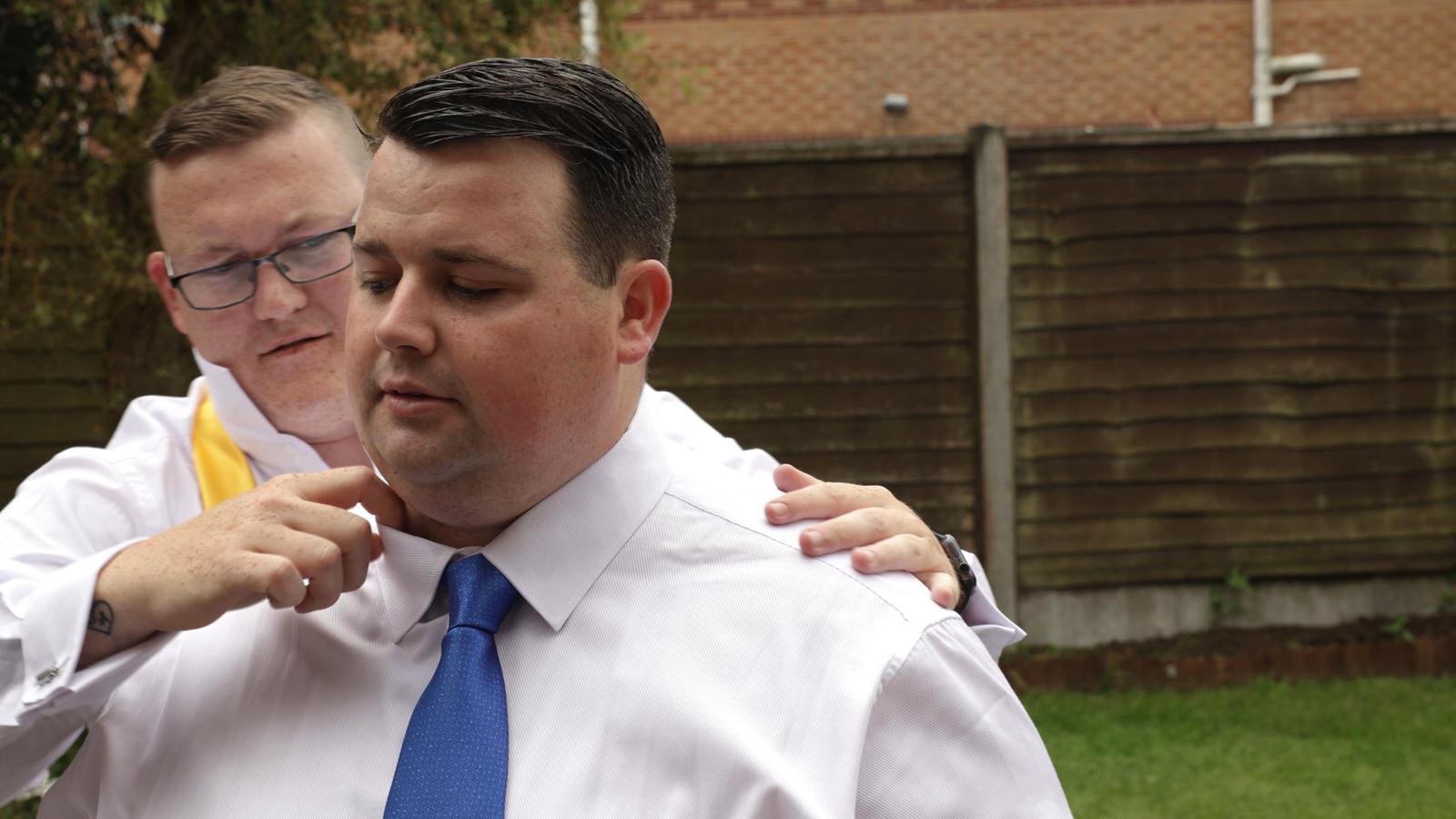 friend helps groom with tie and collar