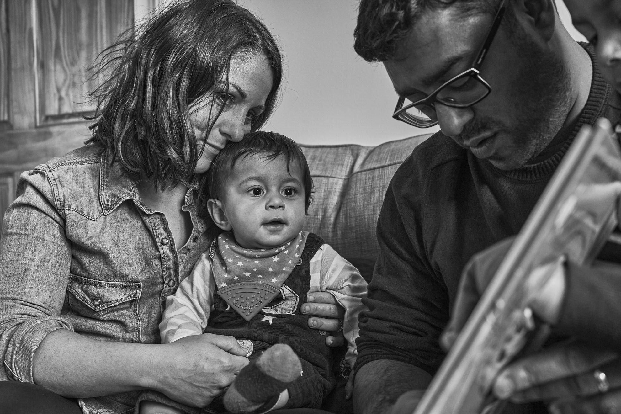 a natural photo of mum cuddling in to her baby whilst dad reads a book
