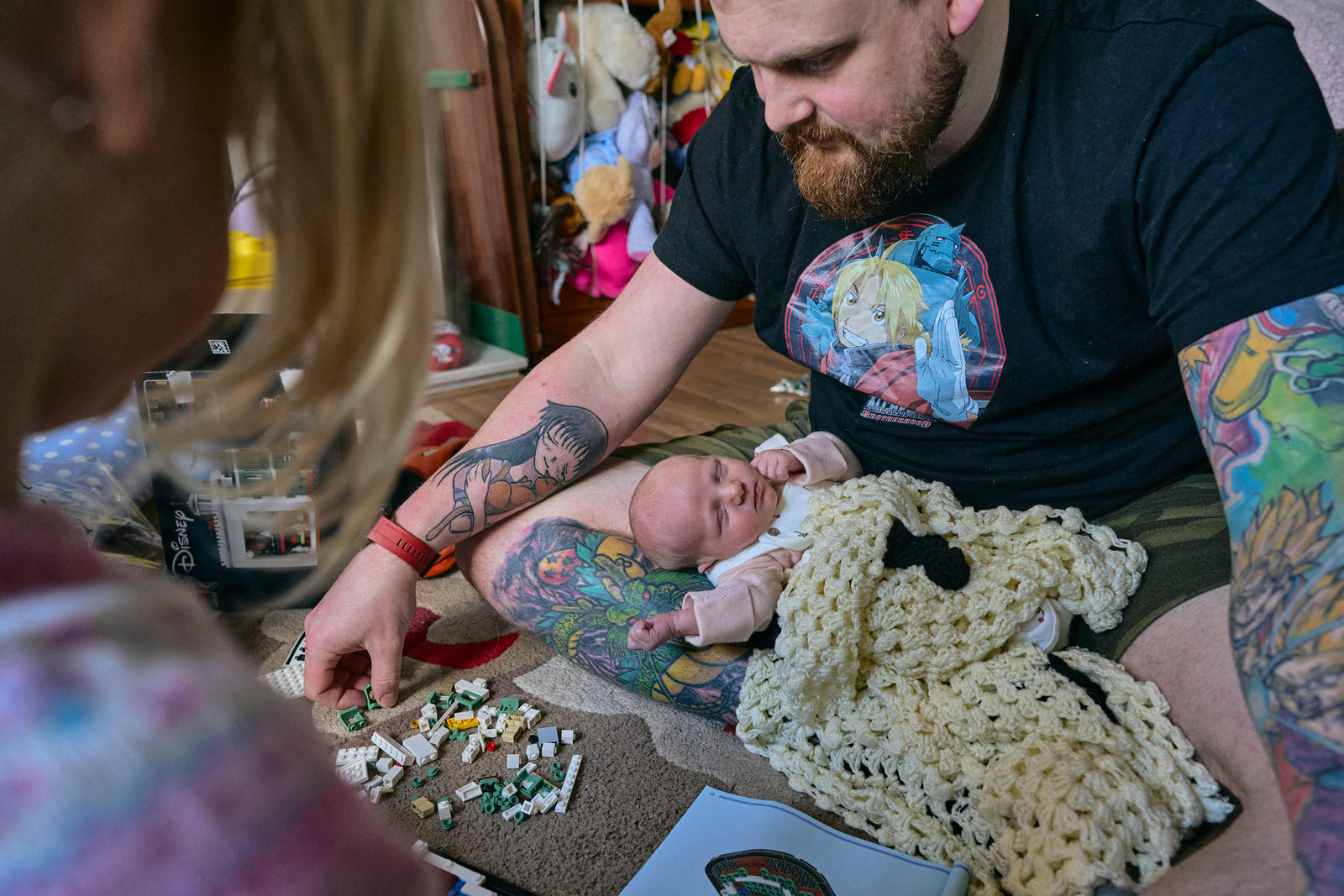 candid relaxed photo of newborn baby asleep on dad playing lego