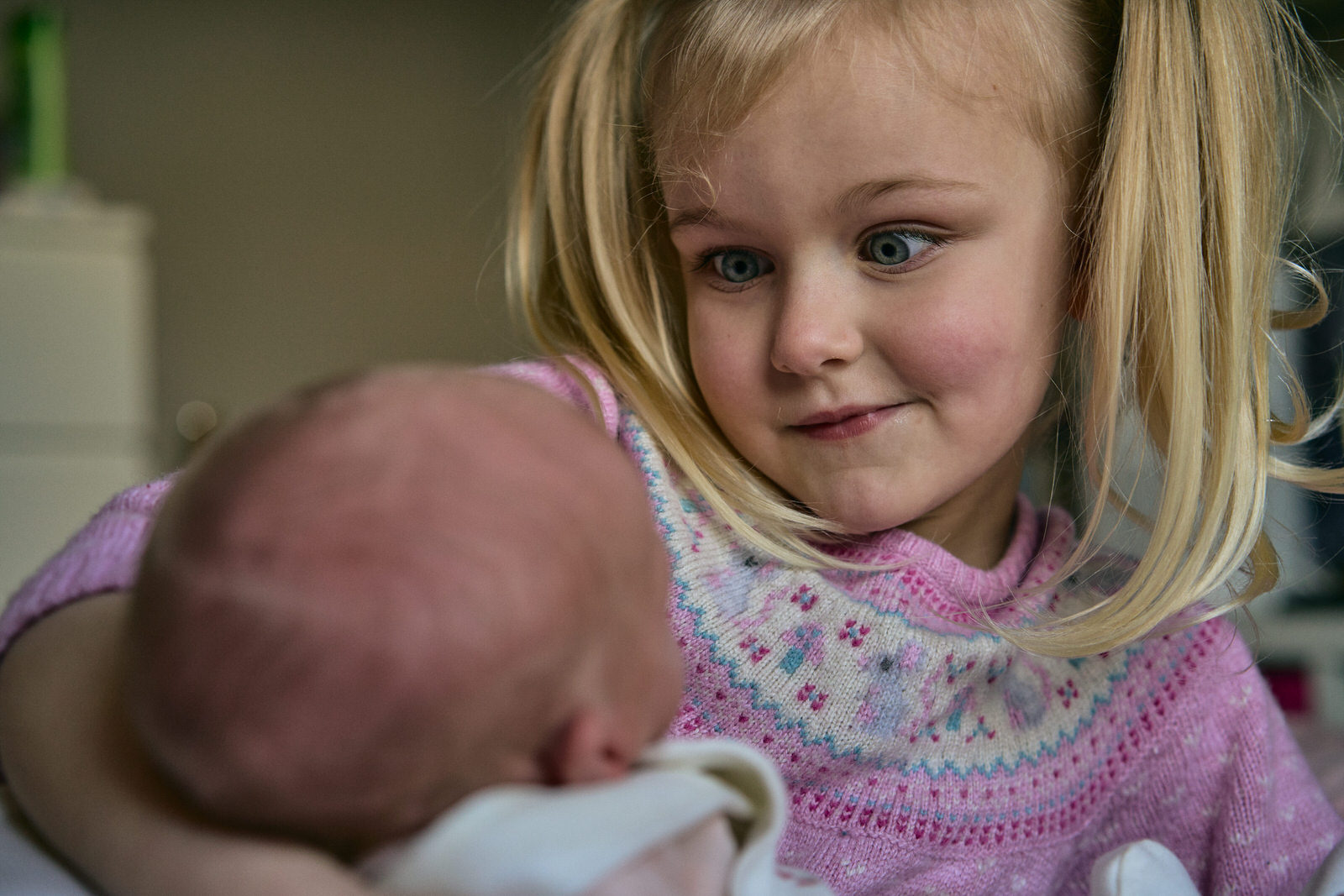 big sister pulls a funny face taking in their new baby sister