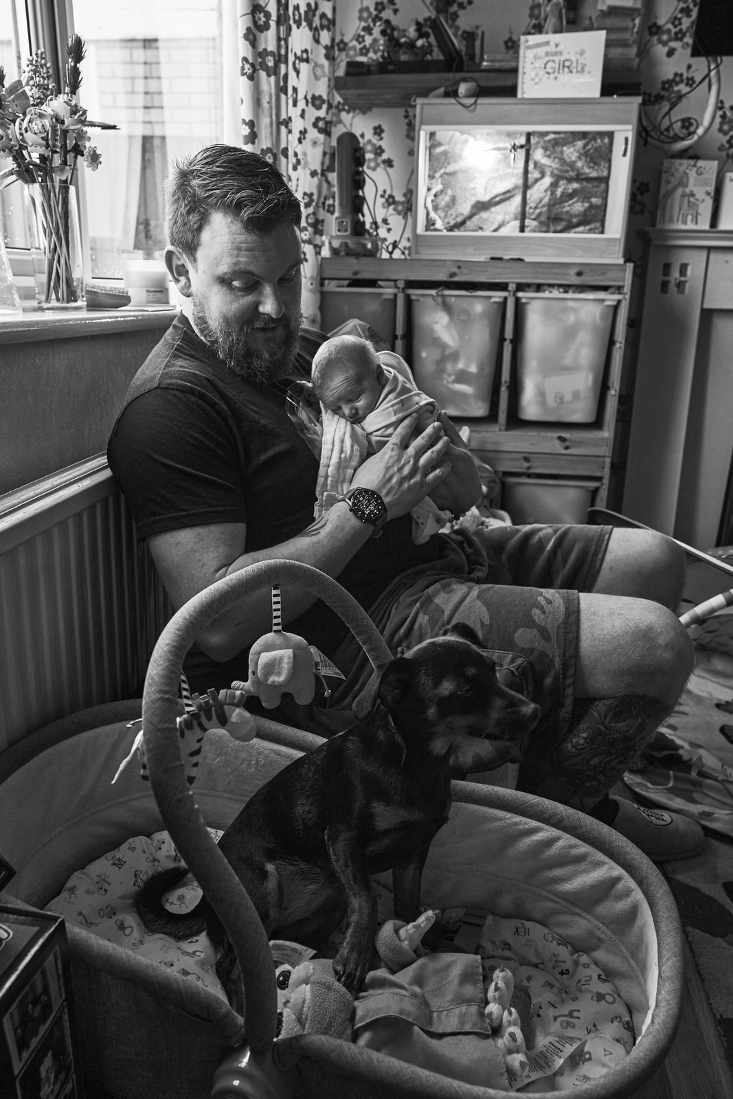 dad holds baby whilst dog sits in the babys cot