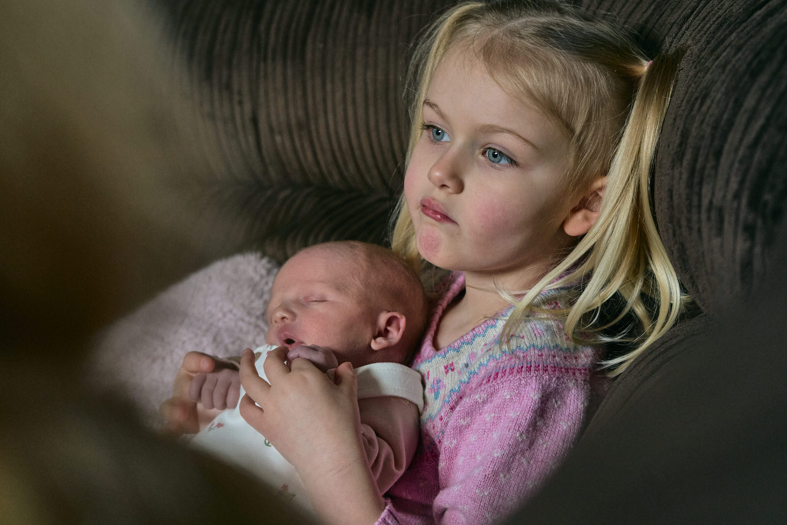 older sibling holds their new baby sister on the sofa