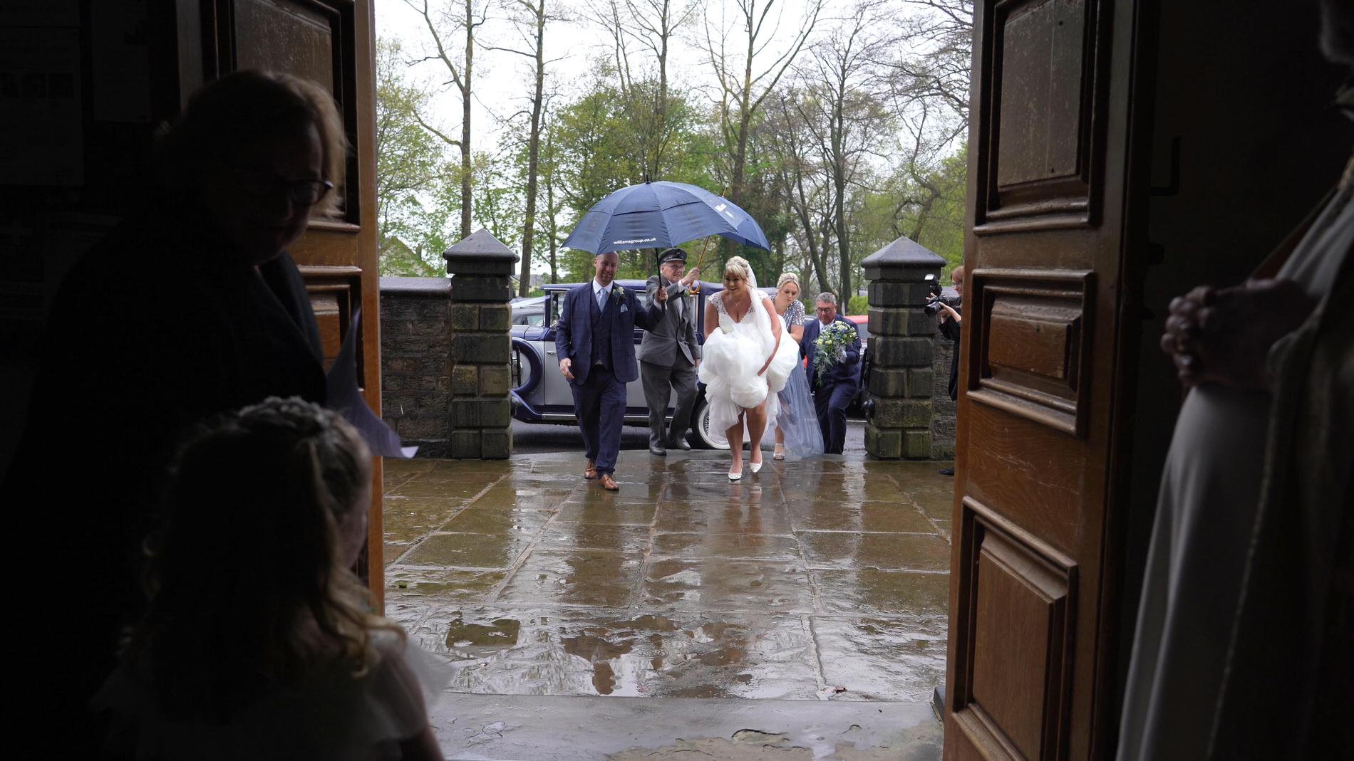 a videographer films a bride walking in to St gregory's church in Weld Bank