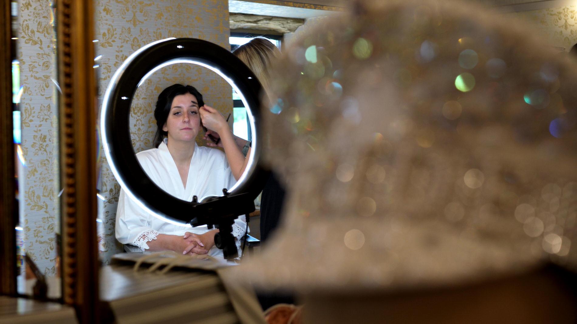 bride gets her makeup done in front of a light ring