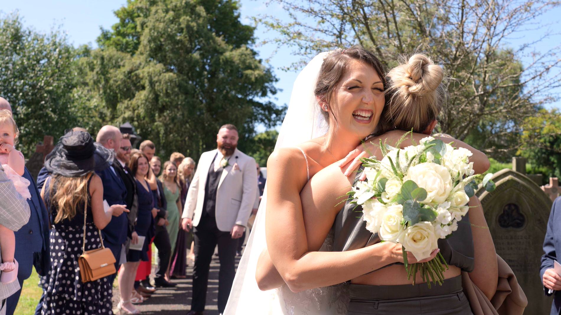 the bride grins and hugs a guest outside church