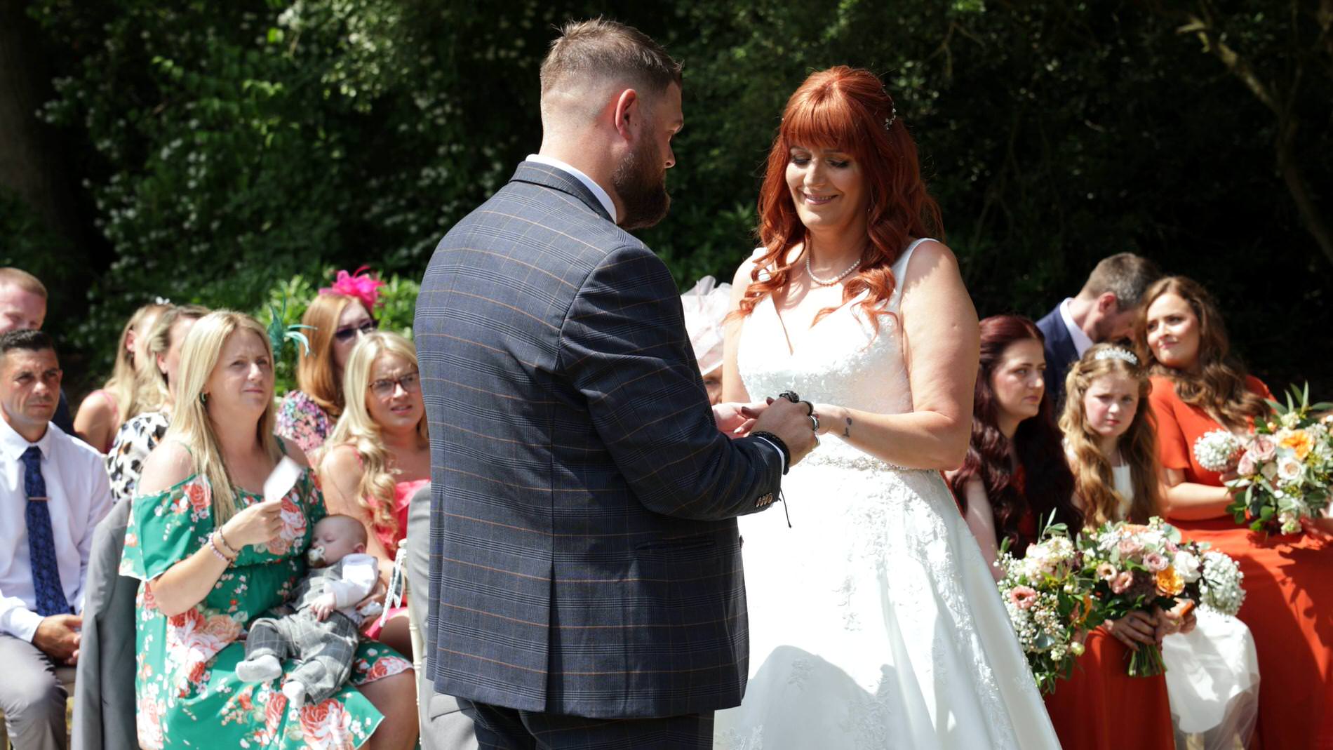 couple exchange wedding rings in the sunshine outside at Nunsmere hall
