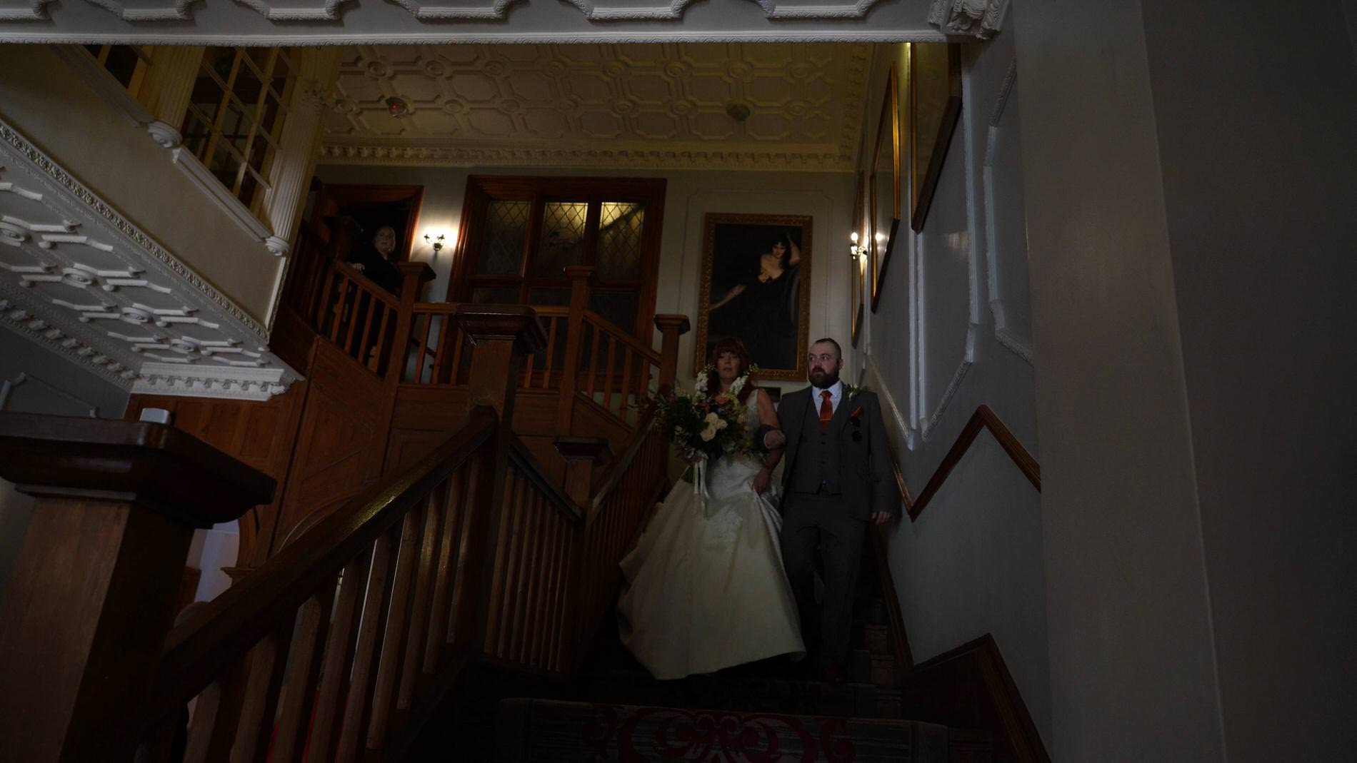 bride walks down the dark Nunsmere hall stairs with her son