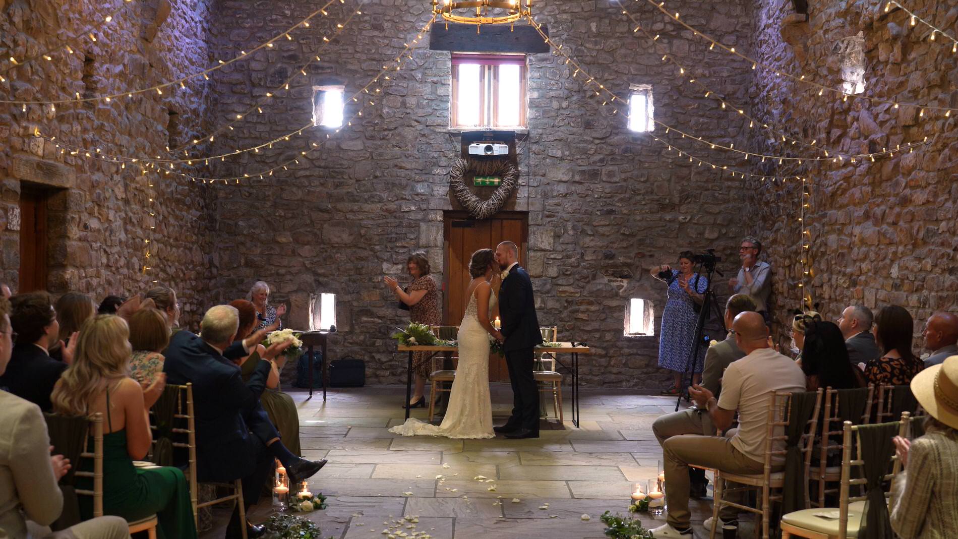 a couple kiss during their wedding ceremony in the tithe barn at Browsholme Hall