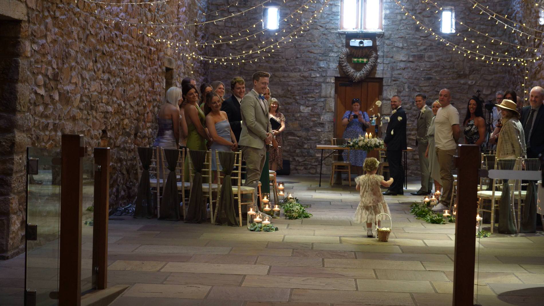 a flower girl walks down the tithe barn aisle at Browsholme Hall