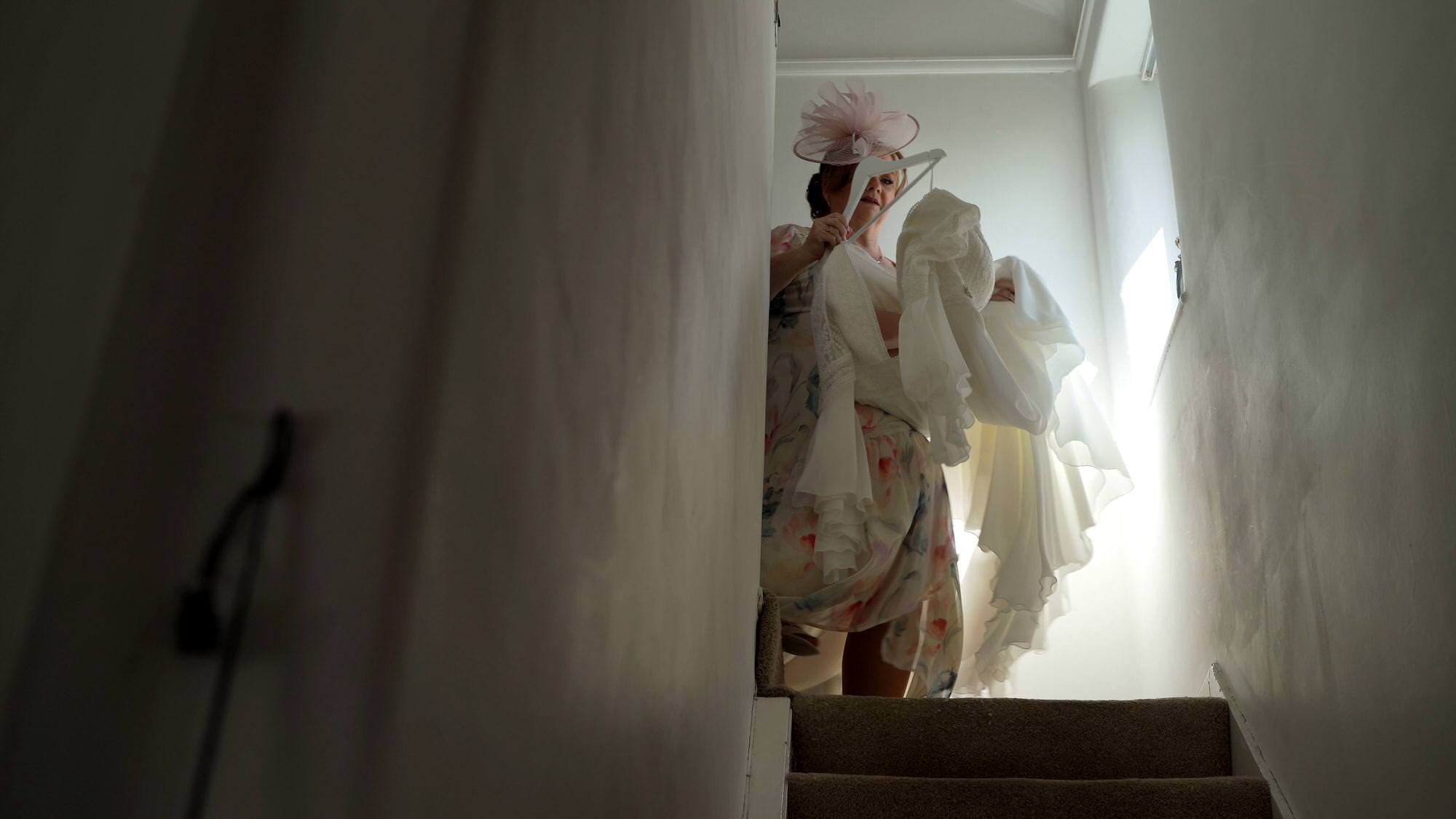 a mother of the bride carries the wedding dress down the stairs