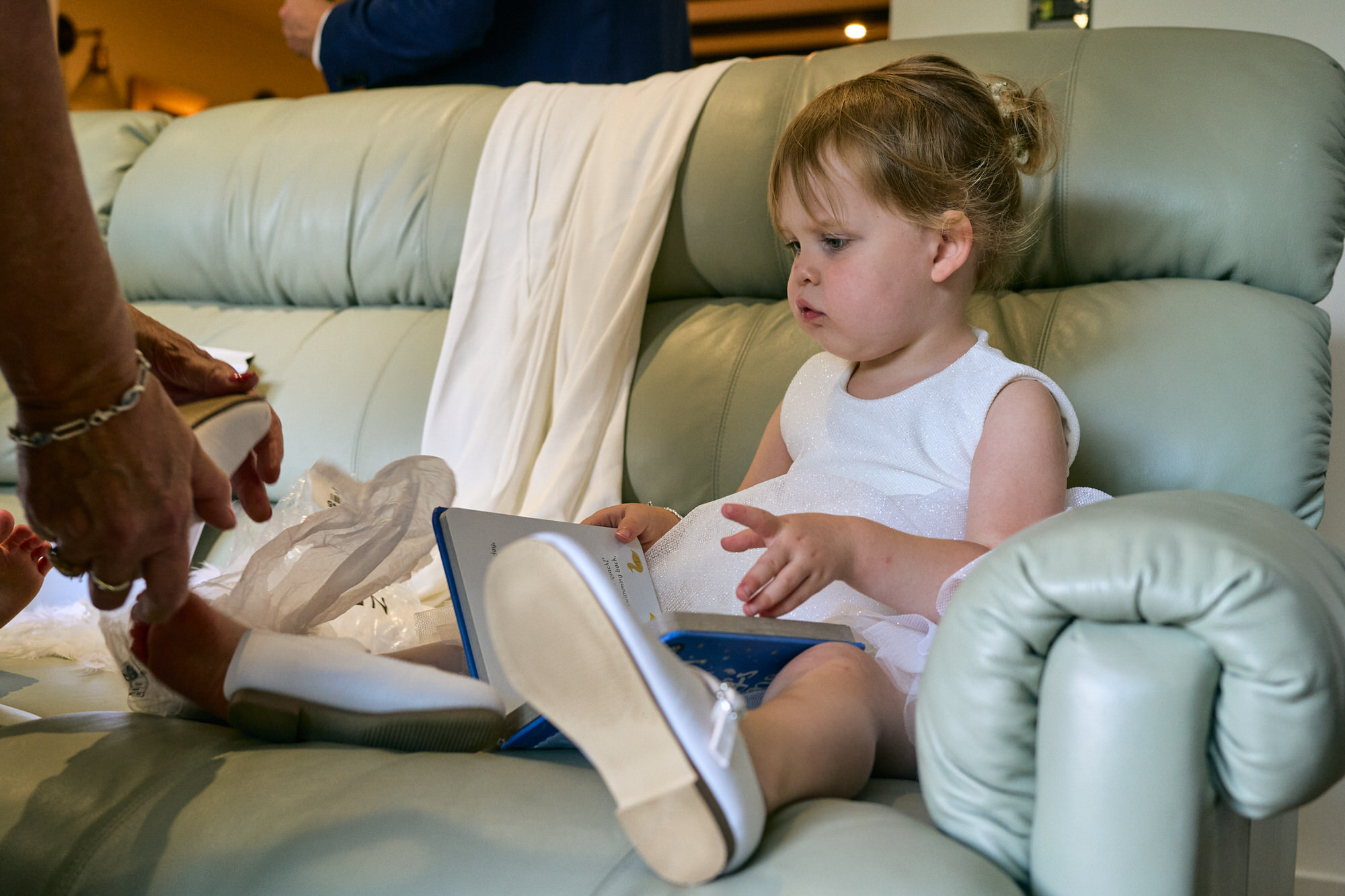 a toddler flowergirl has help with her wedding shoes