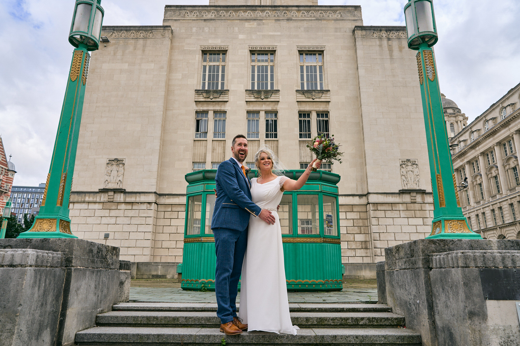 a couple wave to a tour bus a they pose for photos around the Liverpool waterfront