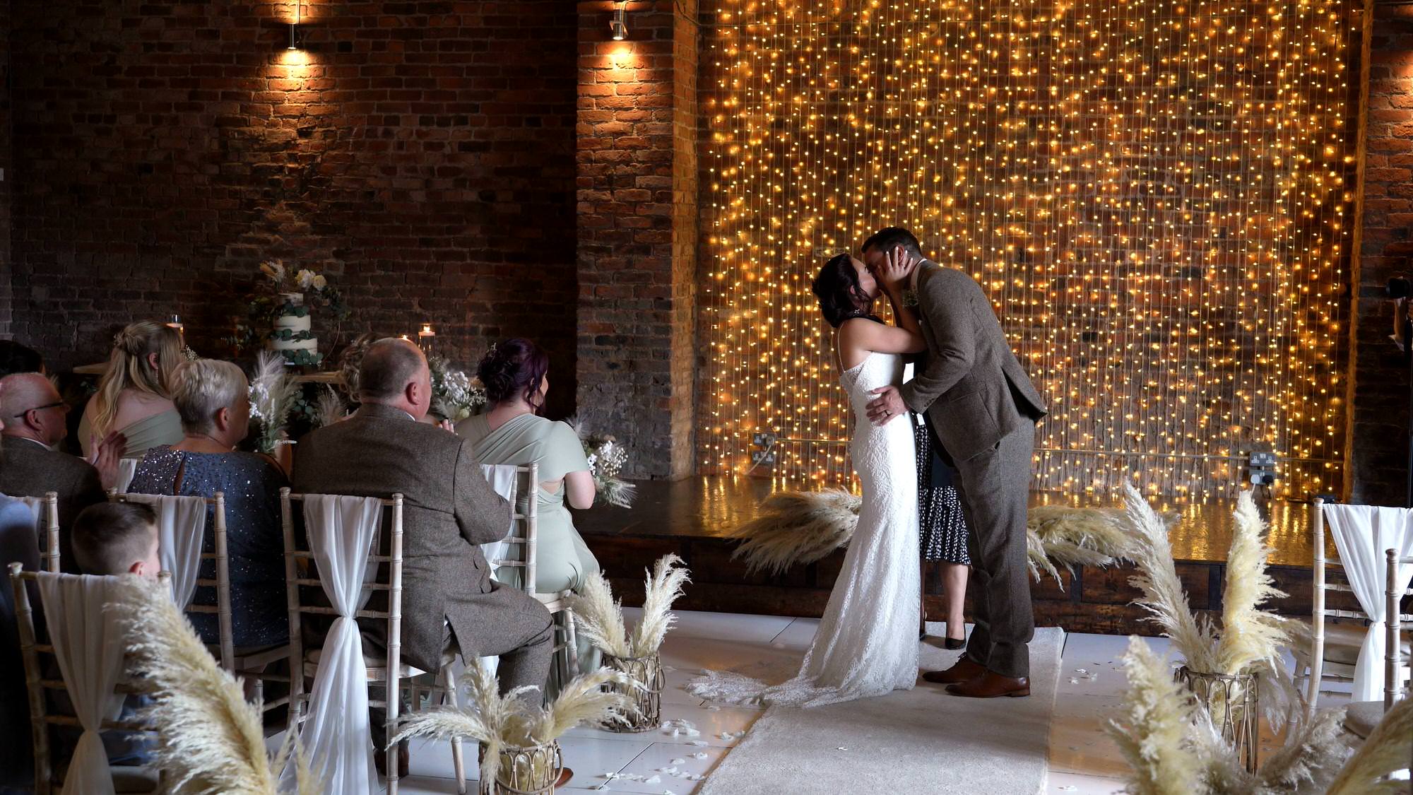 a couple kiss before the wall of fairy lights at the barn at morleys hall