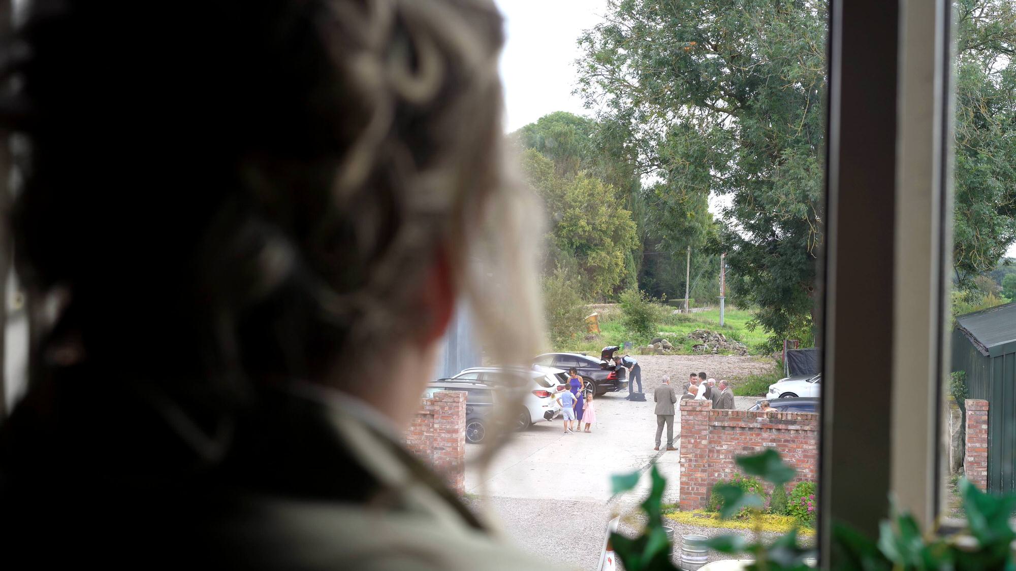 a bridesmaid looks out the window to guests arriving at the barn at morleys hall