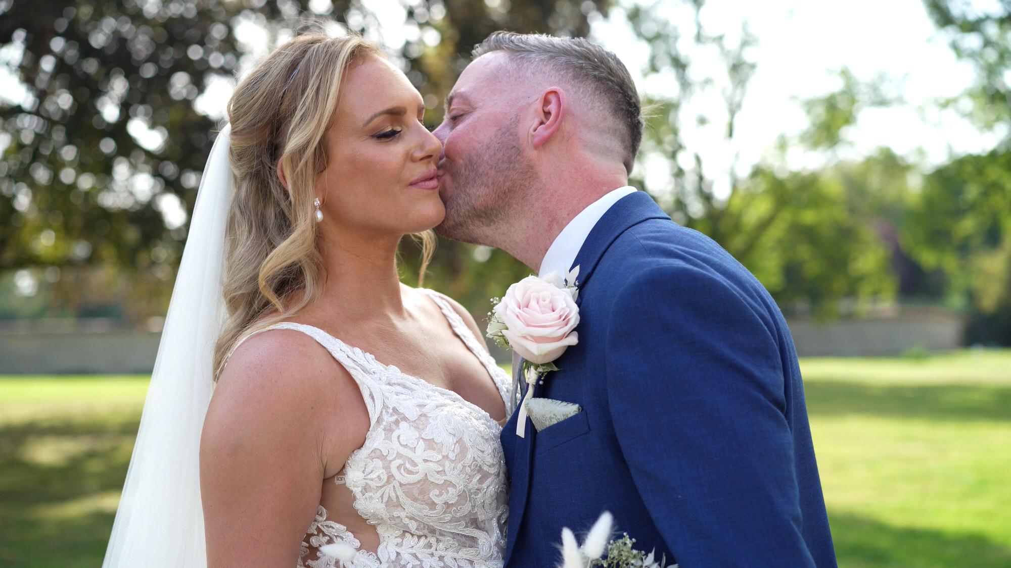 the groom kisses the bride on the cheek in Stubton Hall gardens