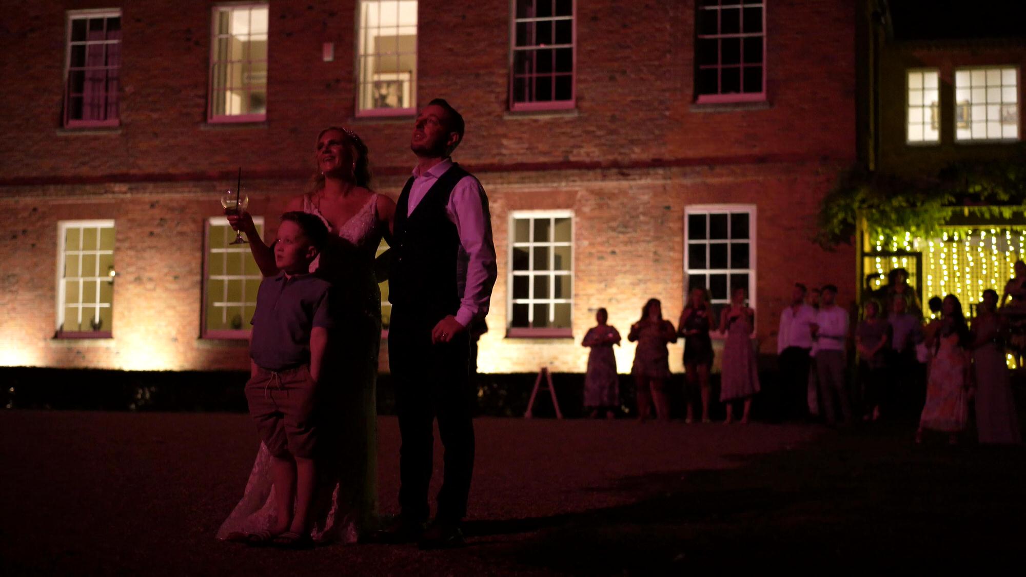 the bride and groom cheer as fireworks light up their faces and Stubton Hall