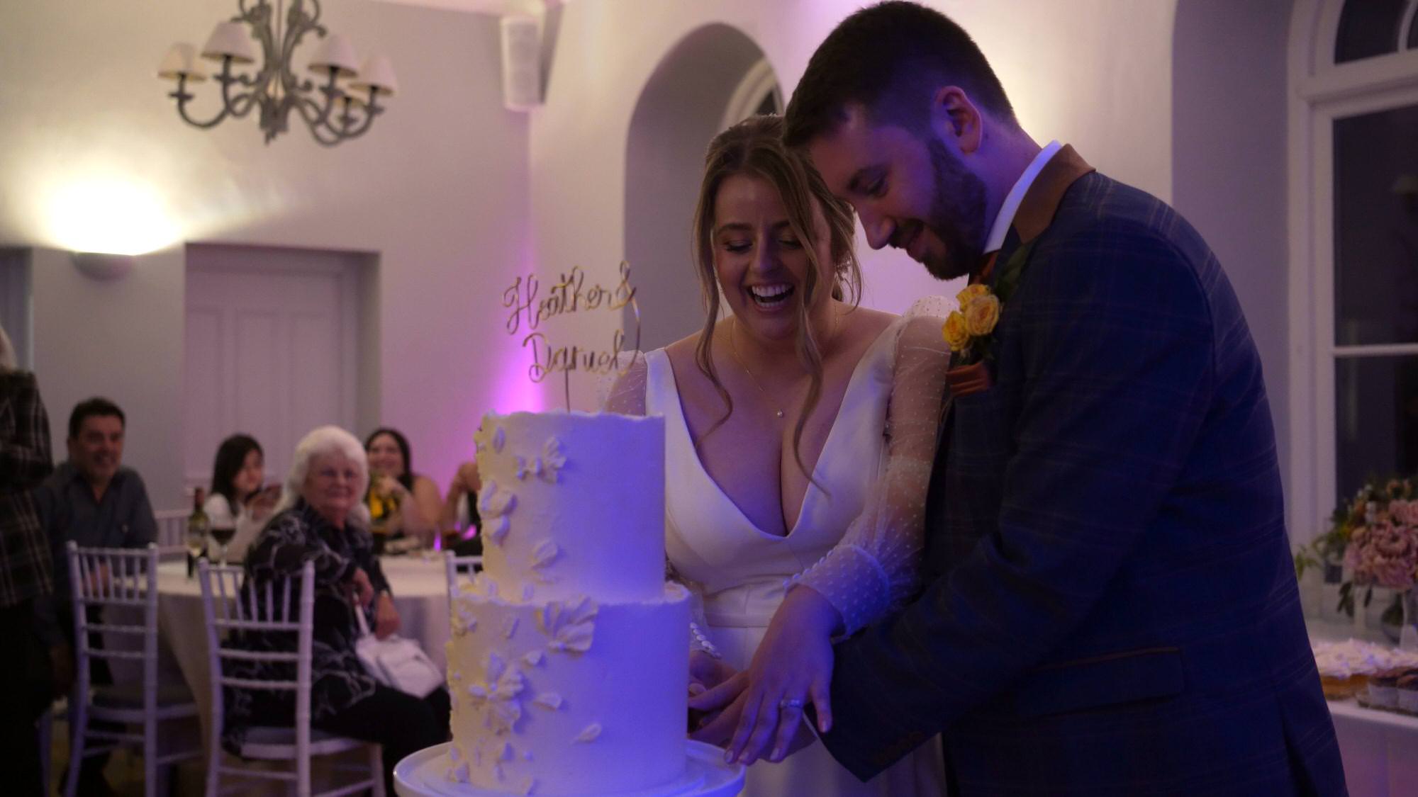 a bride and groom cut their simple white tiered cake at Cartmel Old Grammar