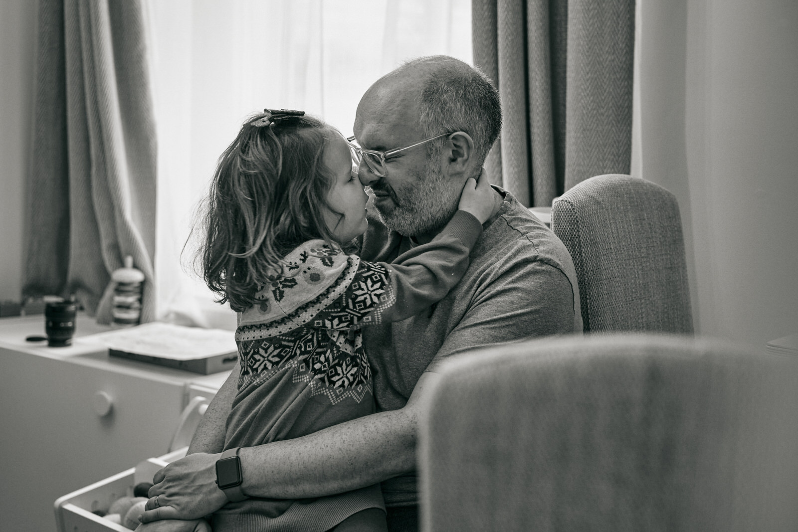a dad snuggles his daughter in a festive Christmas jumper