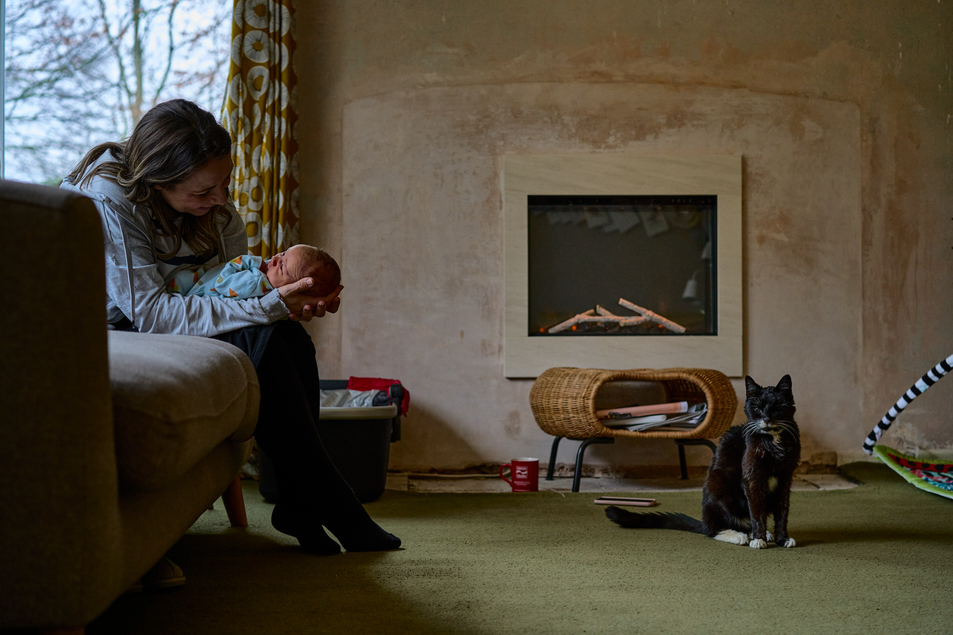 a mum smiles at her baby whilst their pet cat sits closeby