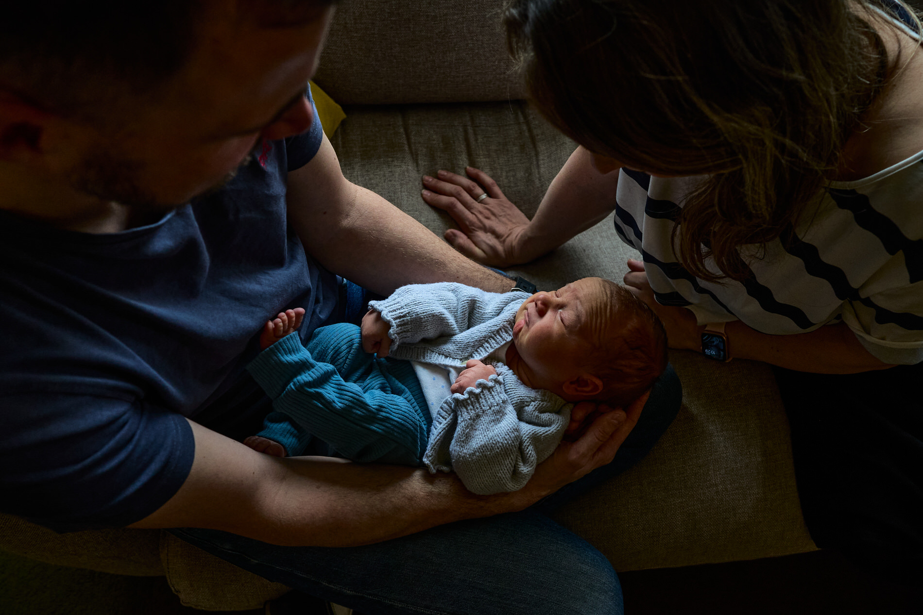 a mum and dad look down at baby with some beautiful natural light at home
