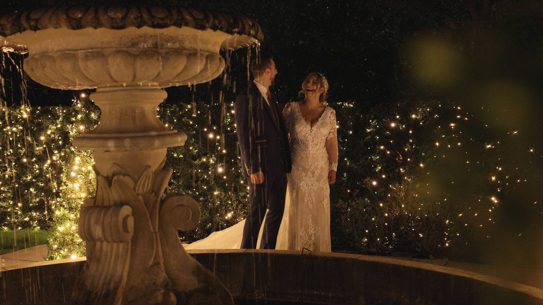 a couple stand by the fountain and fairylights outside Manor House Lindley