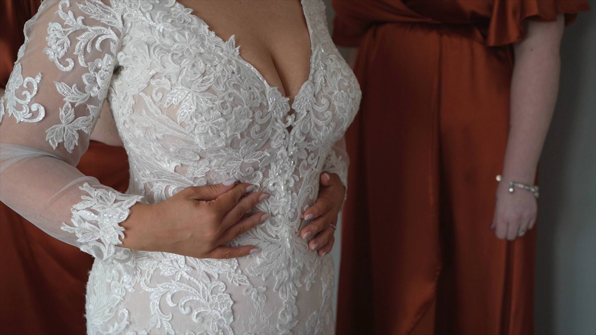 a close up video still of a bride getting in to her wedding dress with sleeves