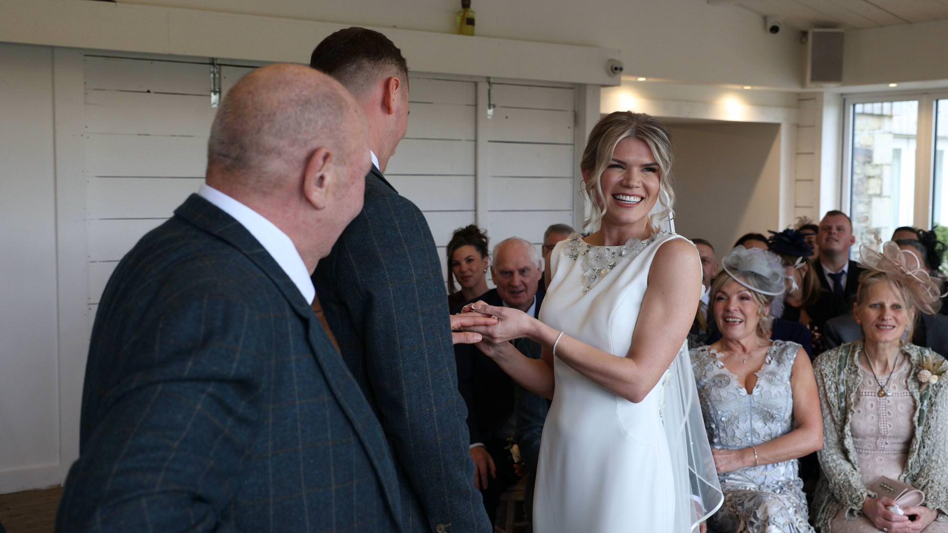 the bride smiles as she holds her grooms lord of the rings wedding ring