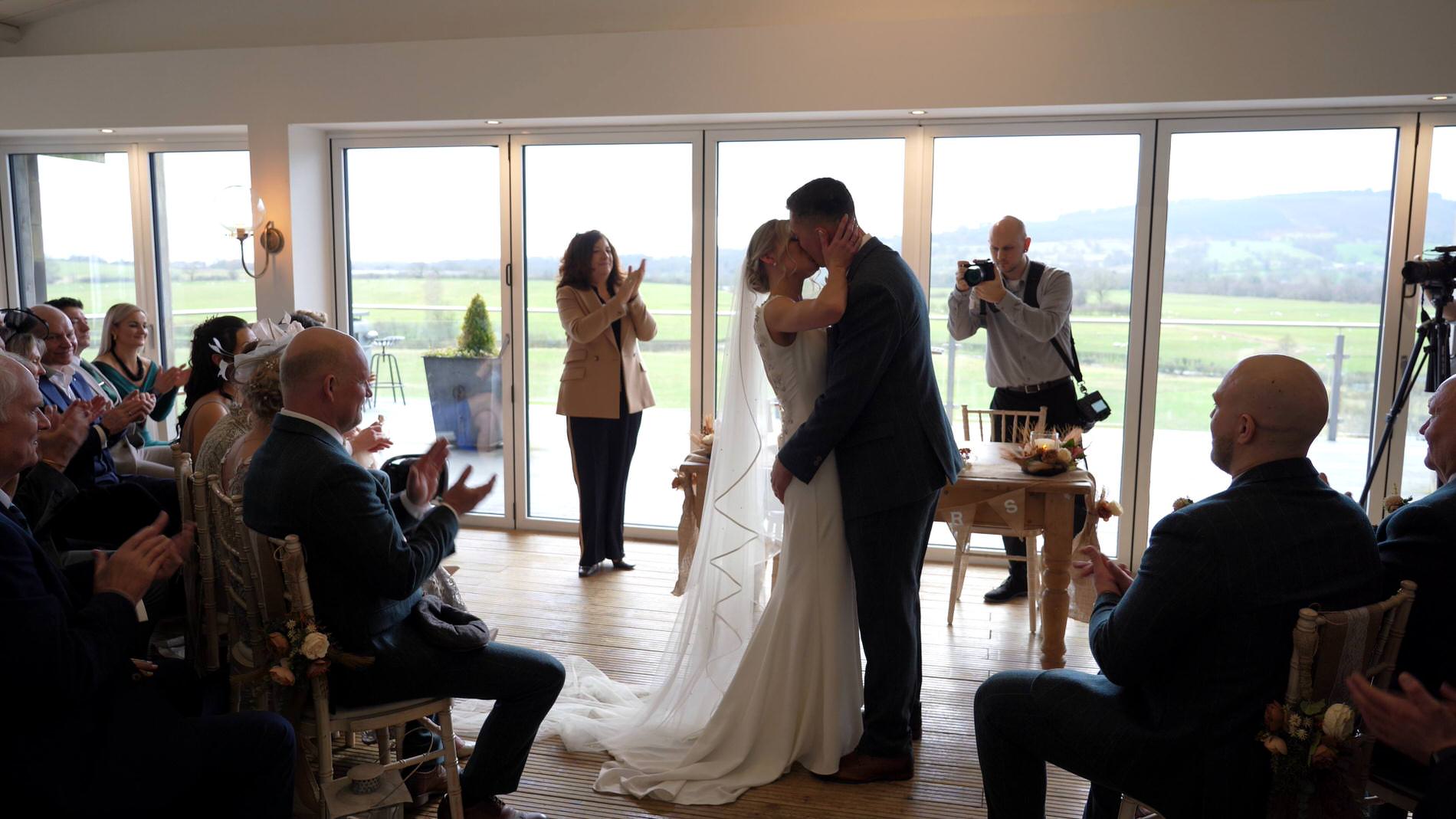 the couple kiss in front of the panoramic views at Bashall Barn