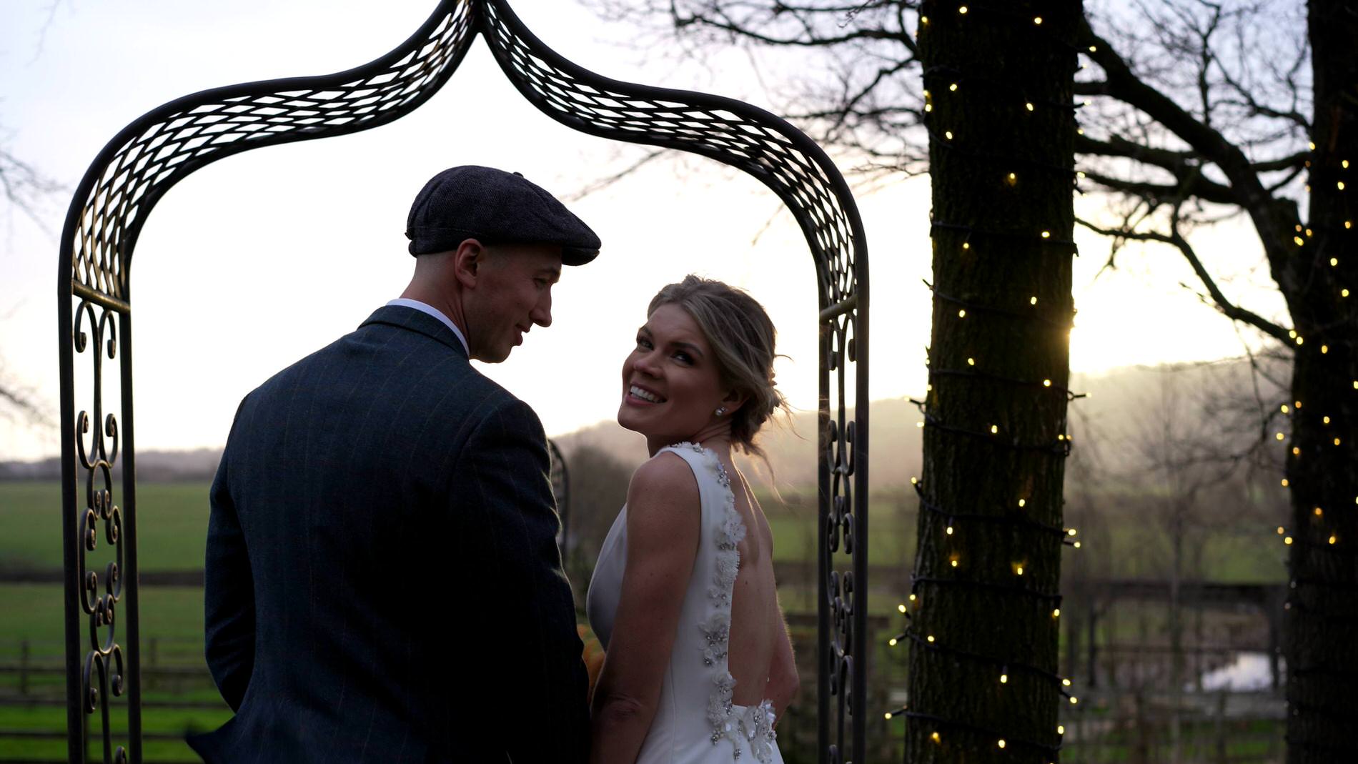 the bride glances back at the videographer as they walk for photos outside Bashall