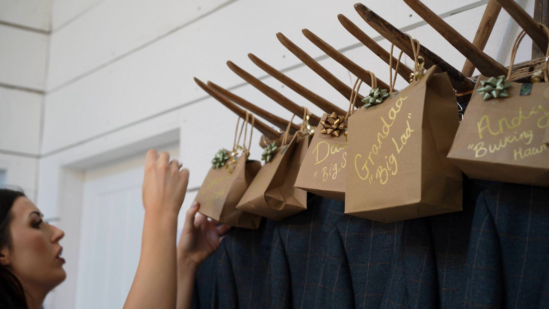 a bridesmaid hangs the groomsmen gifts by the suits