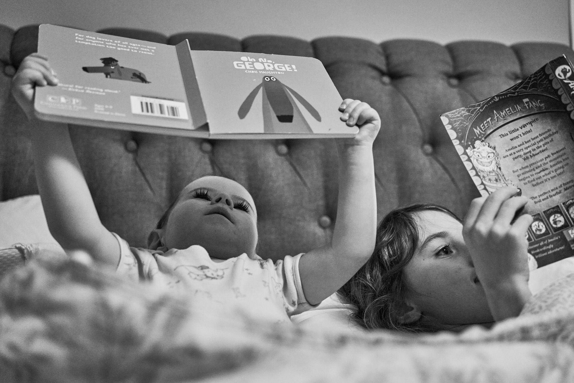 a toddler reads Oh No George in bed with his big sister