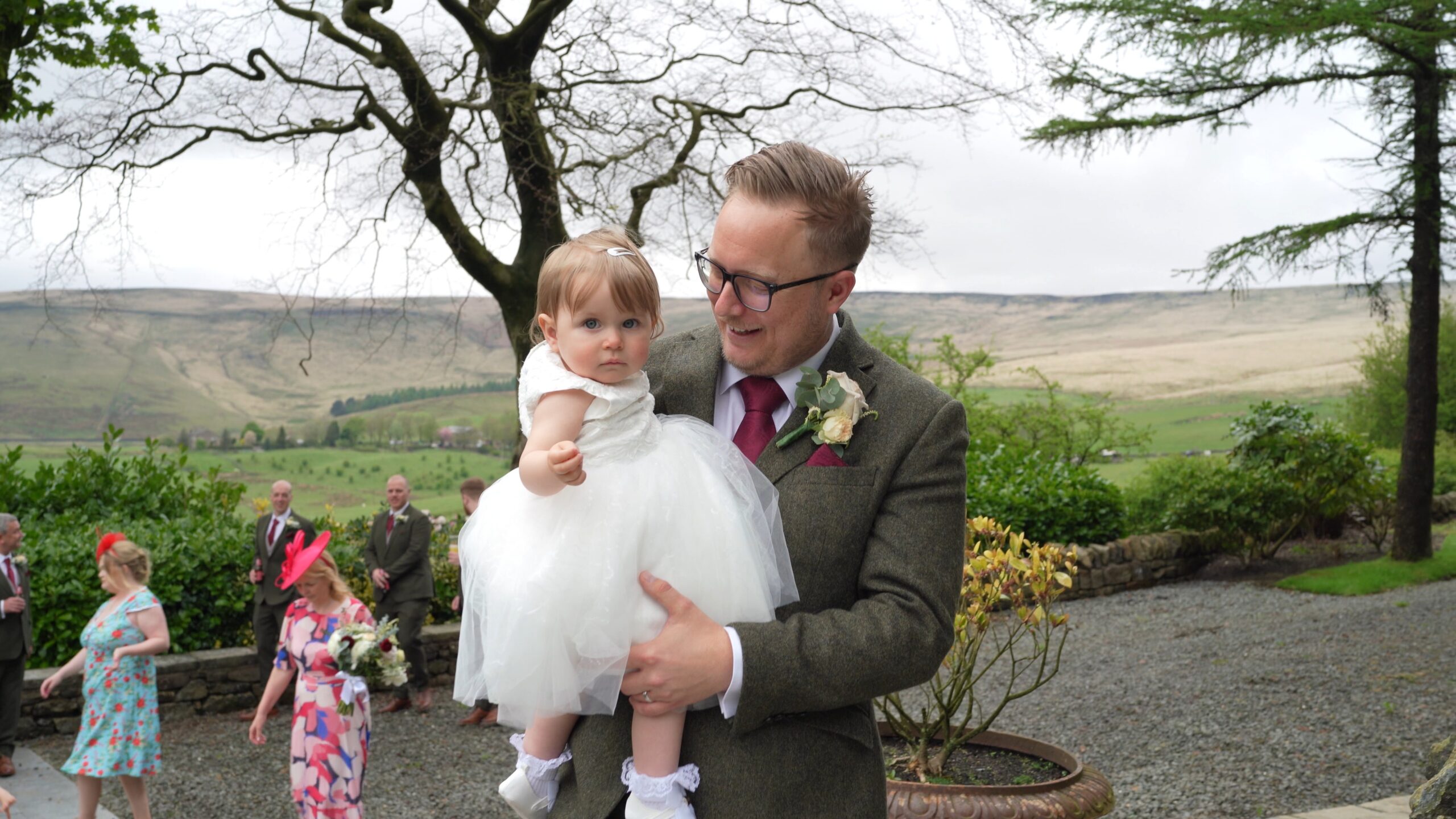the groom carries his flower girl daughter towards the videographer