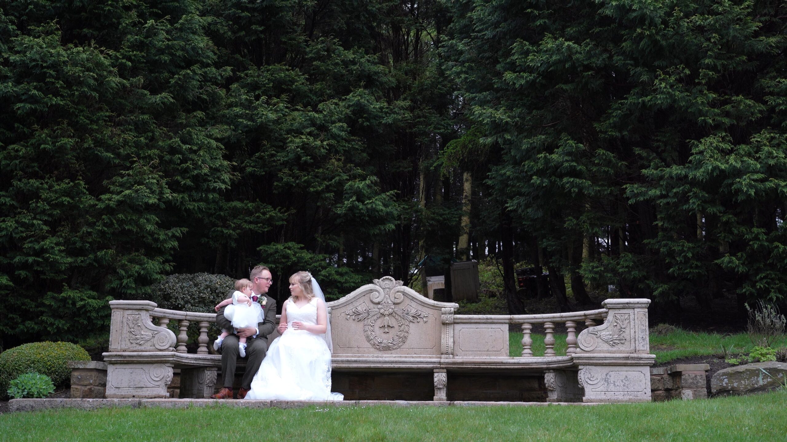 the couple sit with their daughter on a stone bench outside The Saddleworth Hotel
