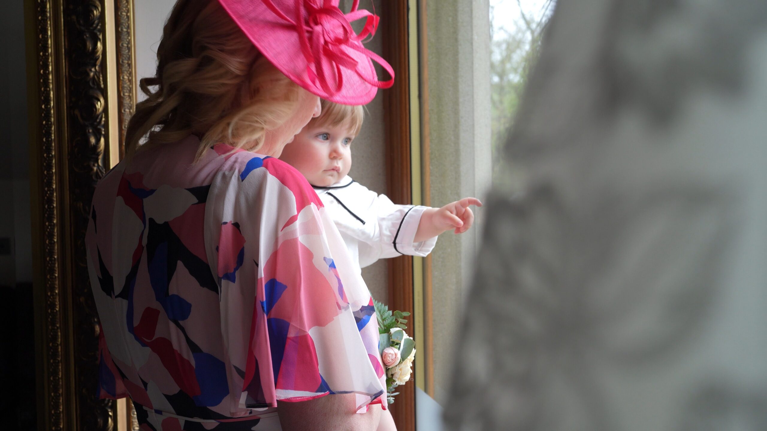 a mother of the bride holds the toddler flowergirl looking out a window at The Saddleworth Hotel