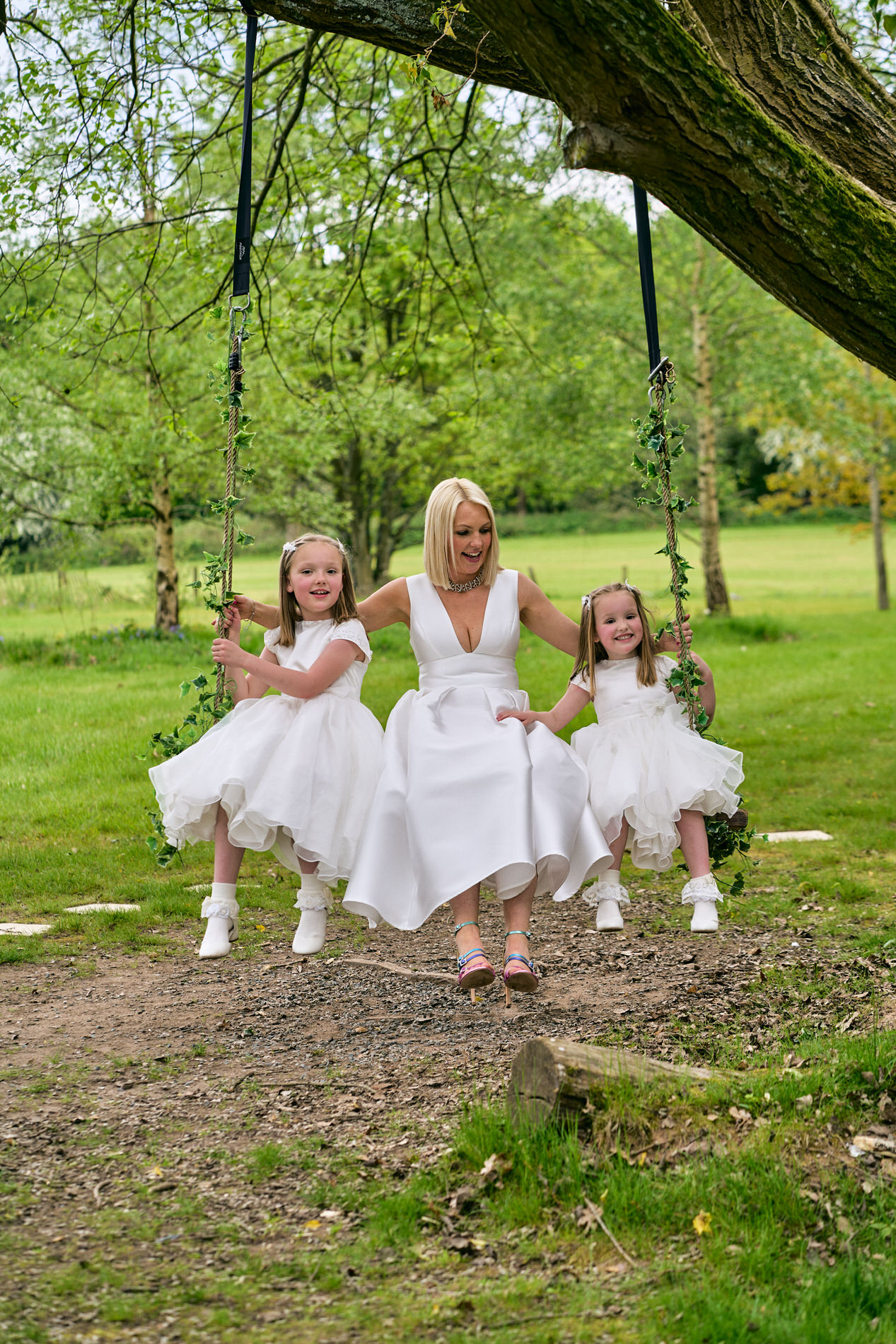 a mum sits with her two daughters on the tree swing outside Holland Hall