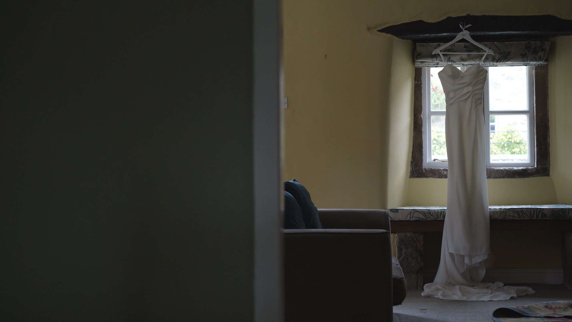 an elegant wedding dress hangs in a window at Browsholme Hall Lancashire