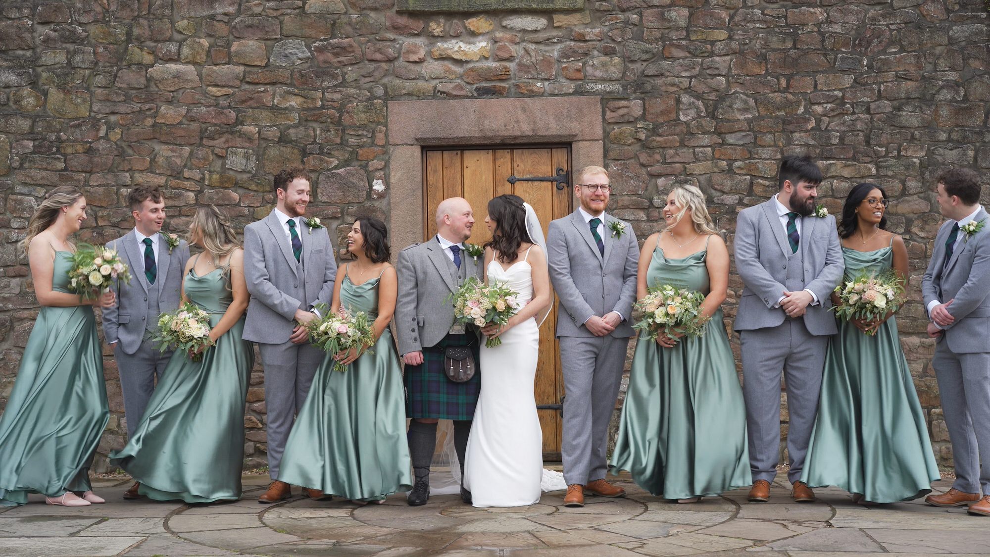 a videographer captures the bridal party posing on a windy day outside Browsholme Hall Lancashire