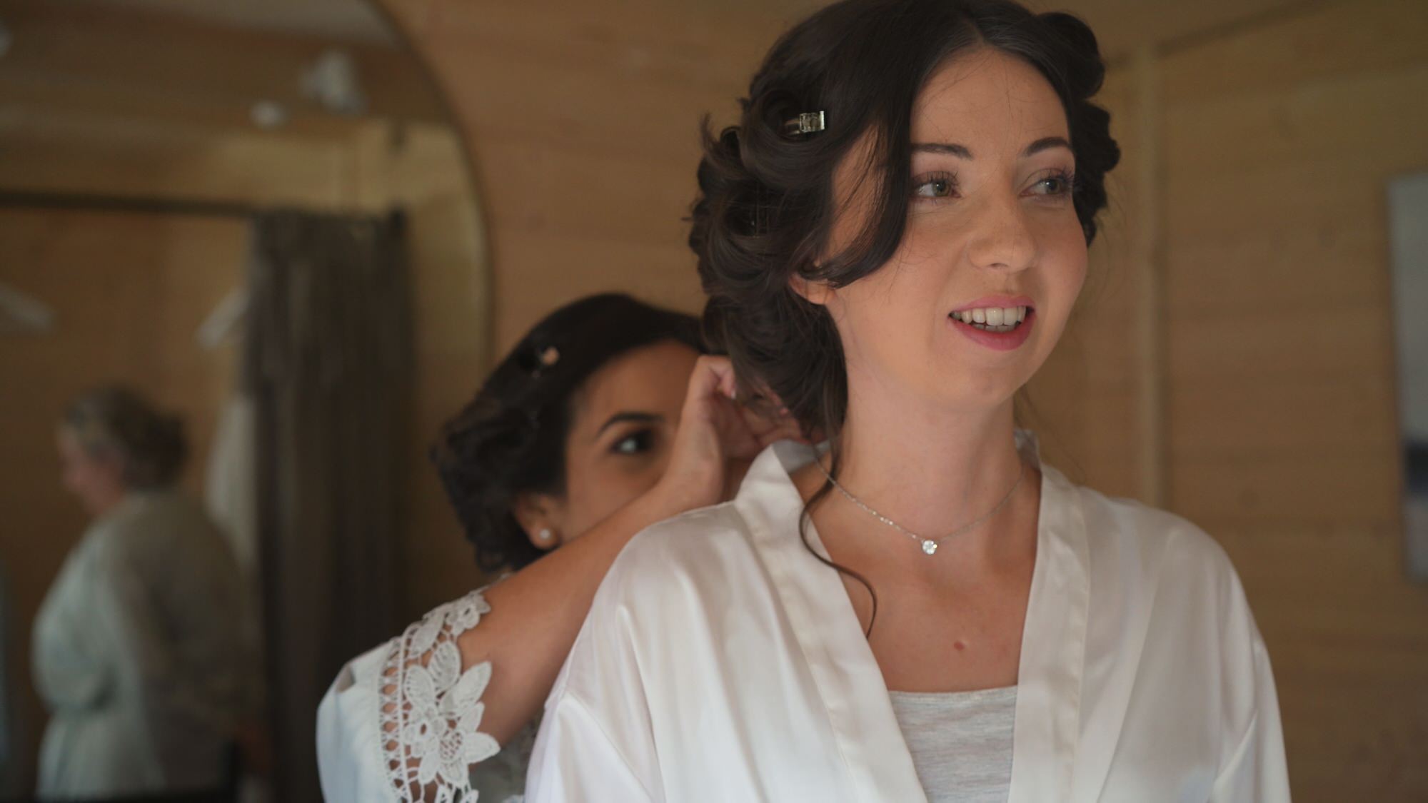 a candid moment of a maid of honour helping with the brides neckalace