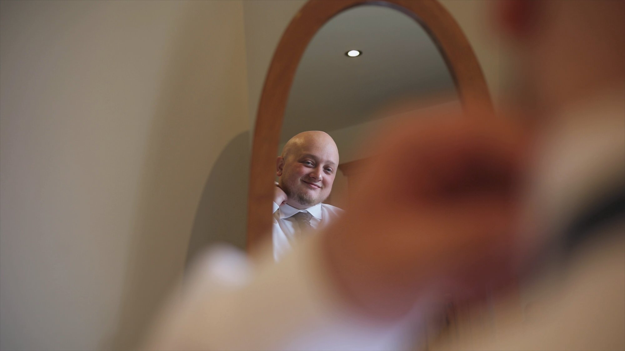 a natural shot of a groom adjusting his tie in a mirror