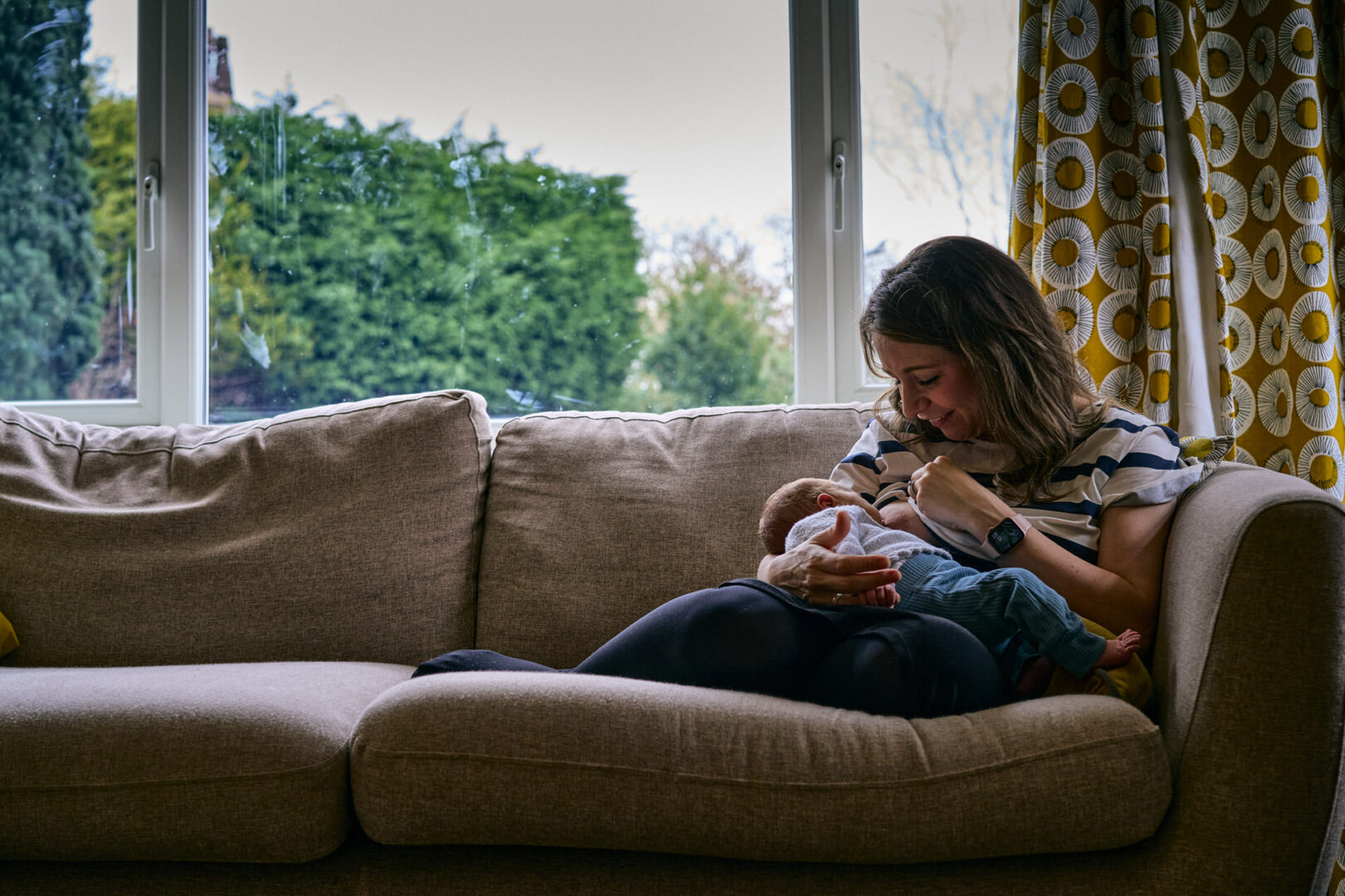 a mum curls up on a chair to breastfeed her newborn baby during a photoshoot in lancashire