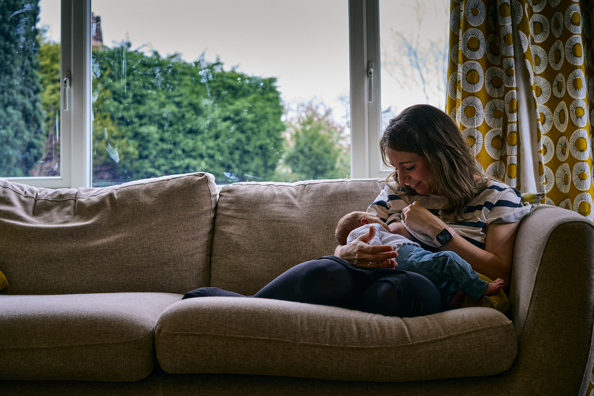 a mum curls up on a chair to breastfeed her newborn baby during a photoshoot in lancashire