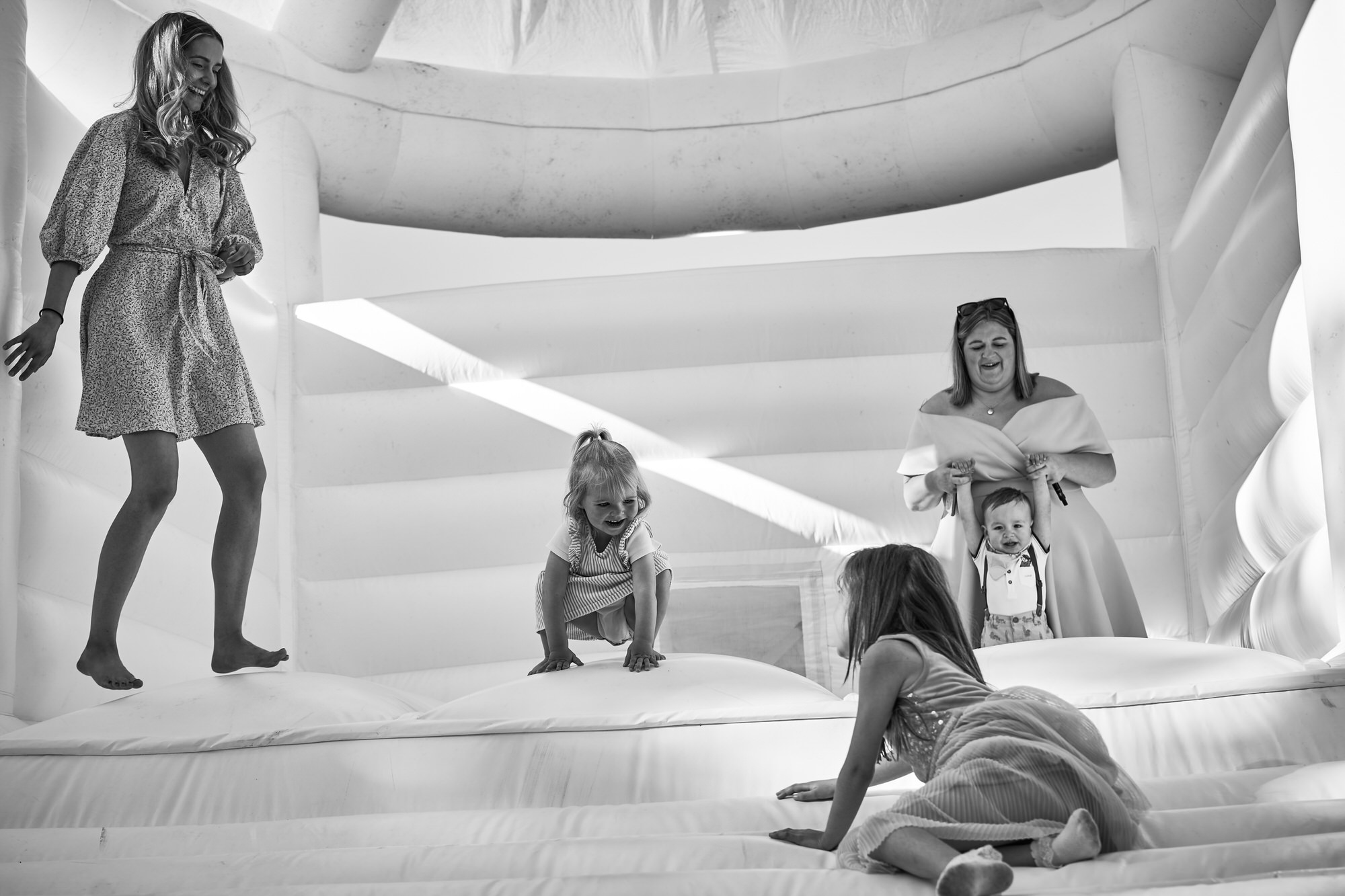 guests and children laugh as they jump on a white bouncy house