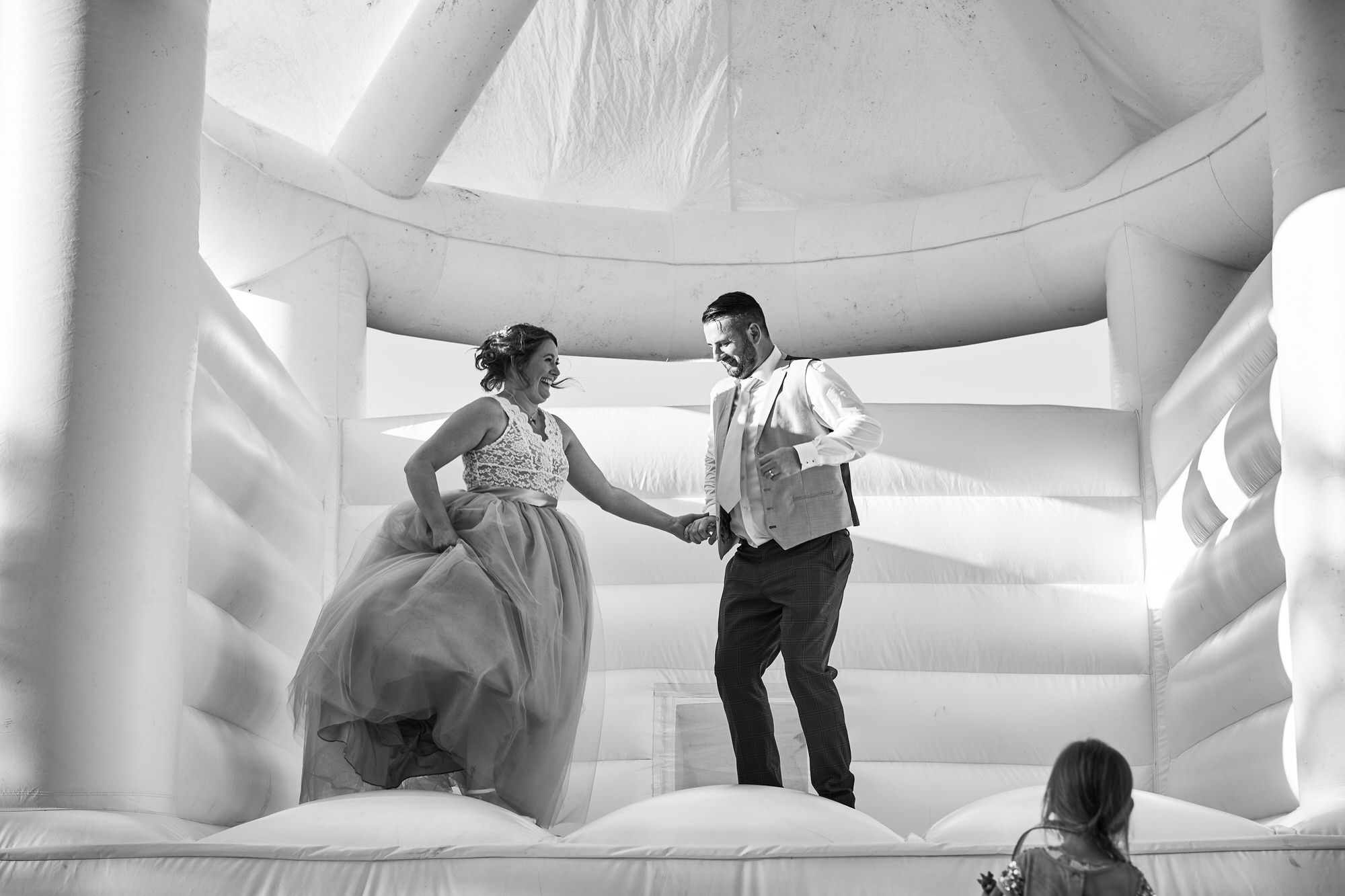 a bride and groom jump on the white bouncy castle