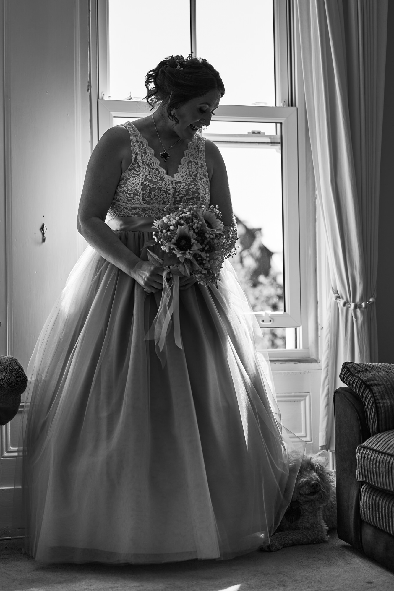a bride laughs as her dog appears behind her wedding dress