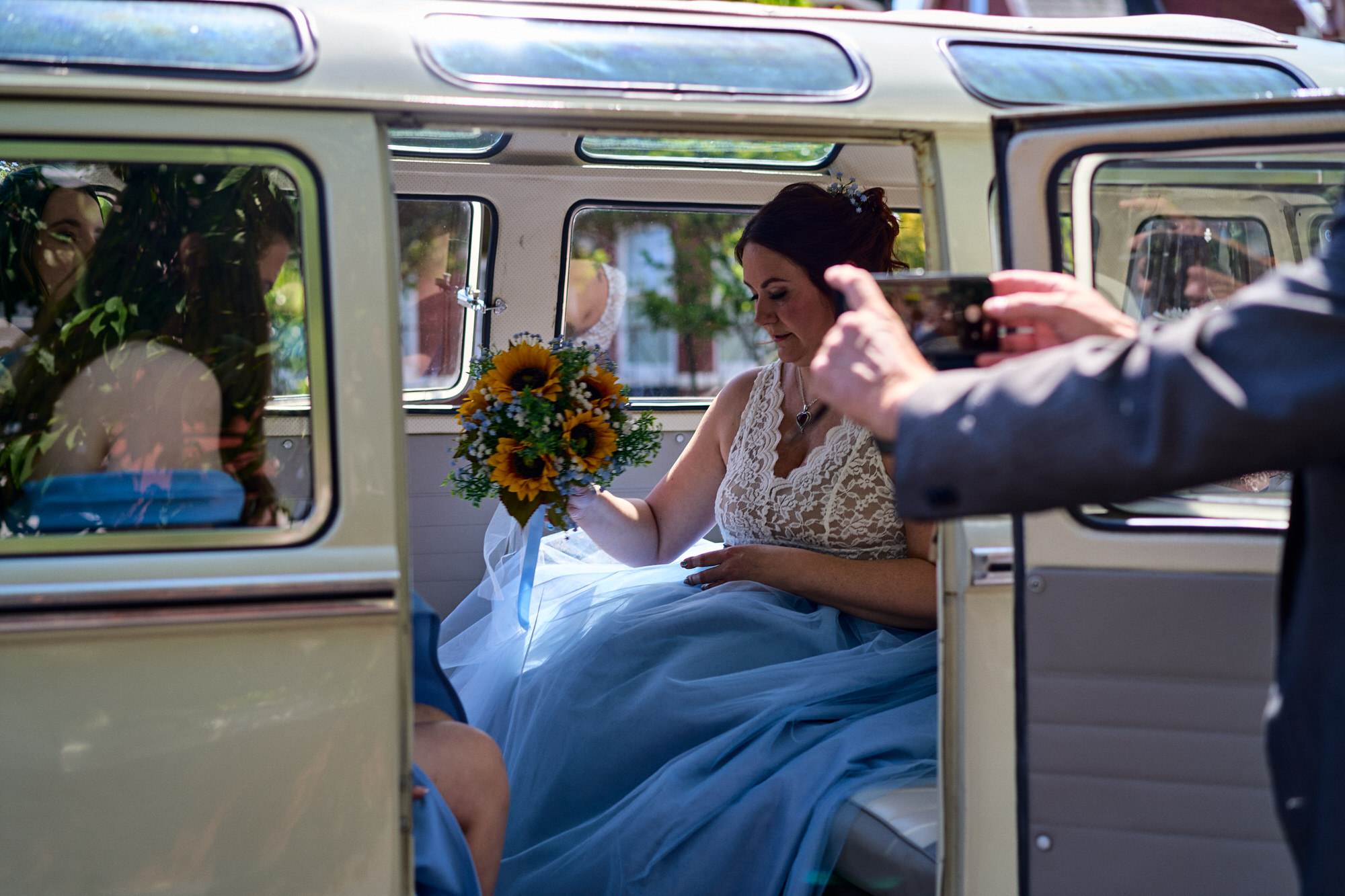 a bride sits in the campervan as the driver takes a phone photo