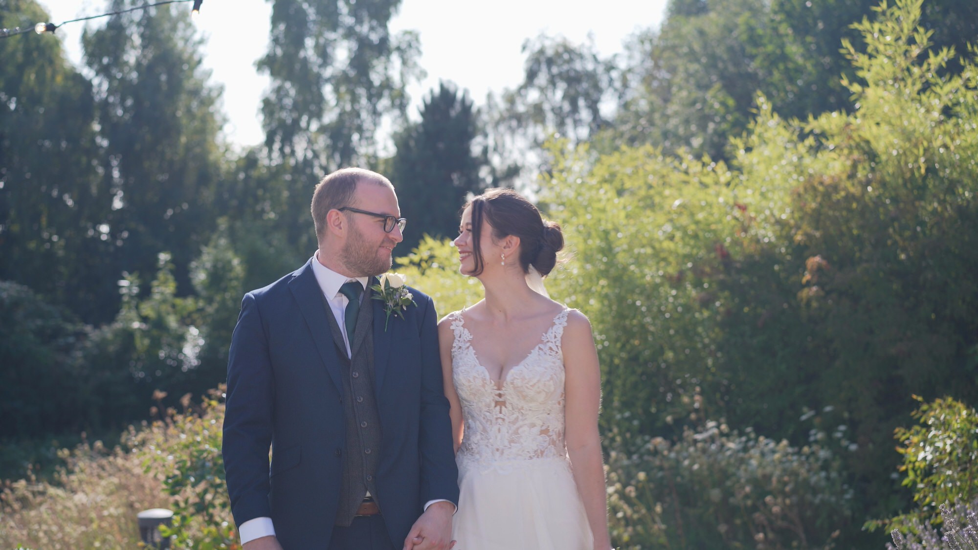a bride and groom smile at each other during natural couples photos outside Sefton Palm House