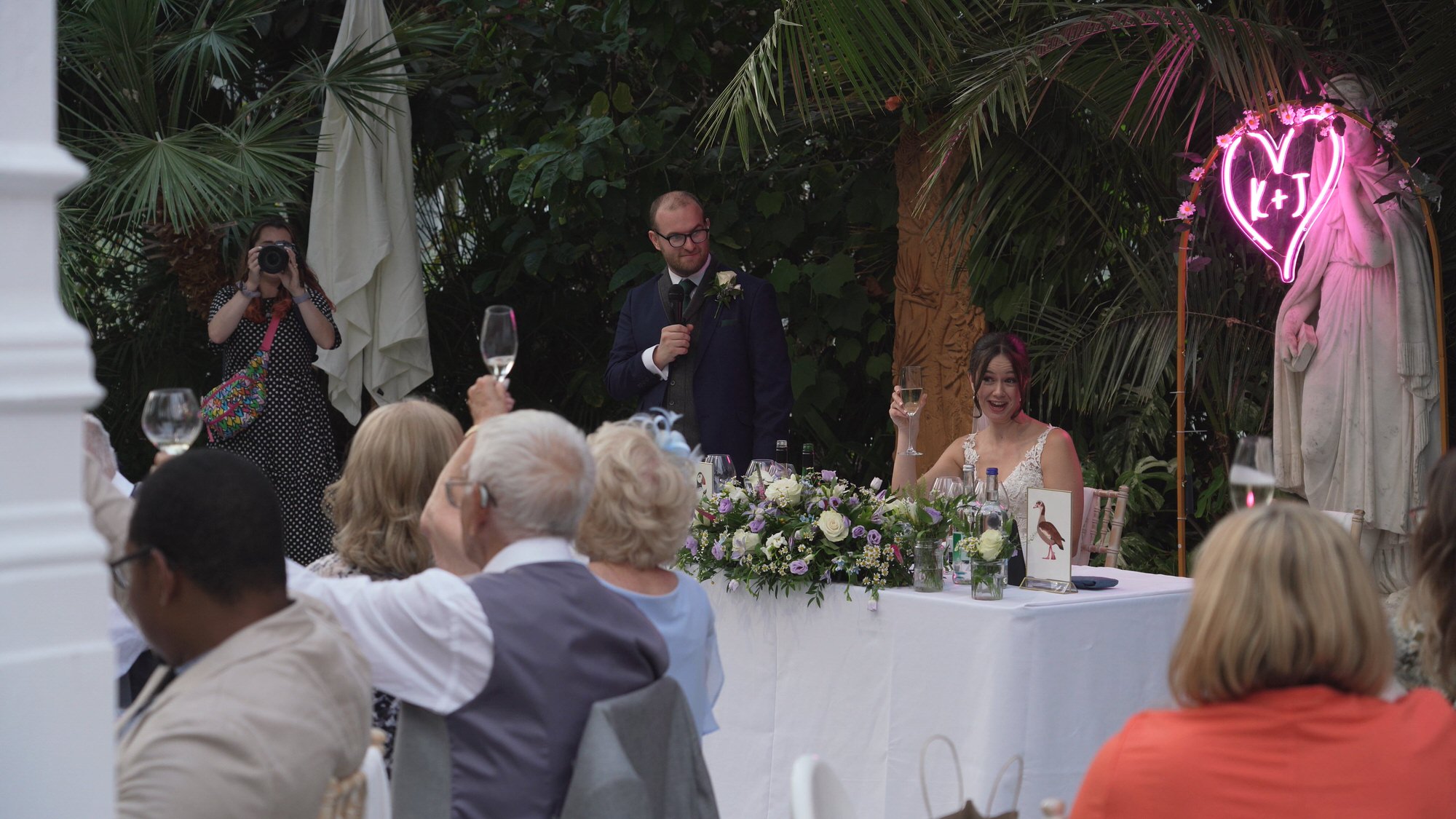 a wide video shot of the bride toasting herself during speeches at Sefton Palm House