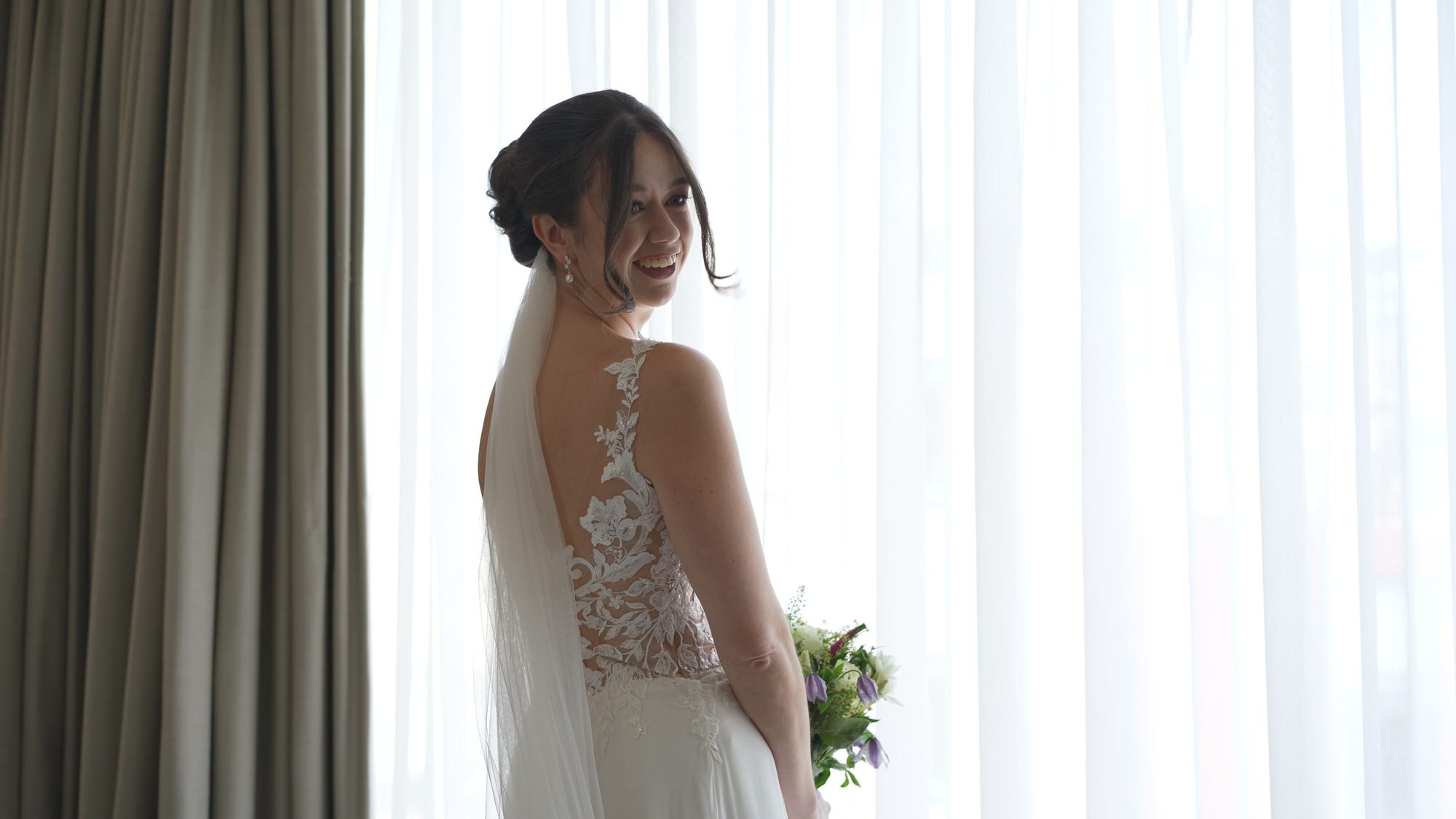 a candid video still of a bride smiling at her bridesmaids in her dress