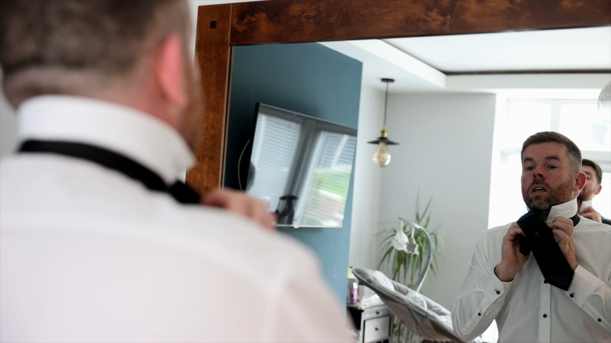 groom ties his wedding tie in a mirror