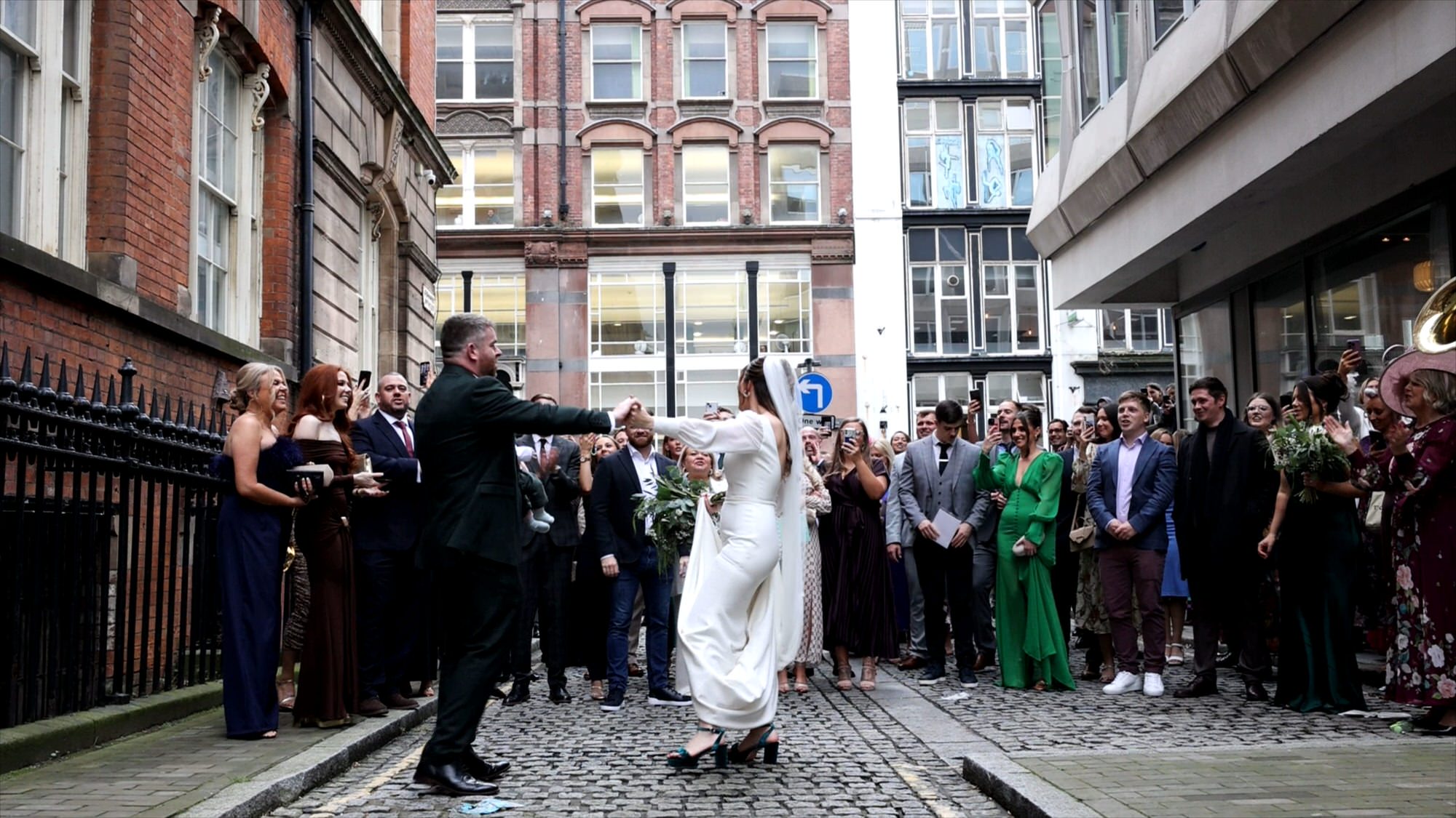 a wide documentary video still of wedding guests dancing with a walking band in Liverpool
